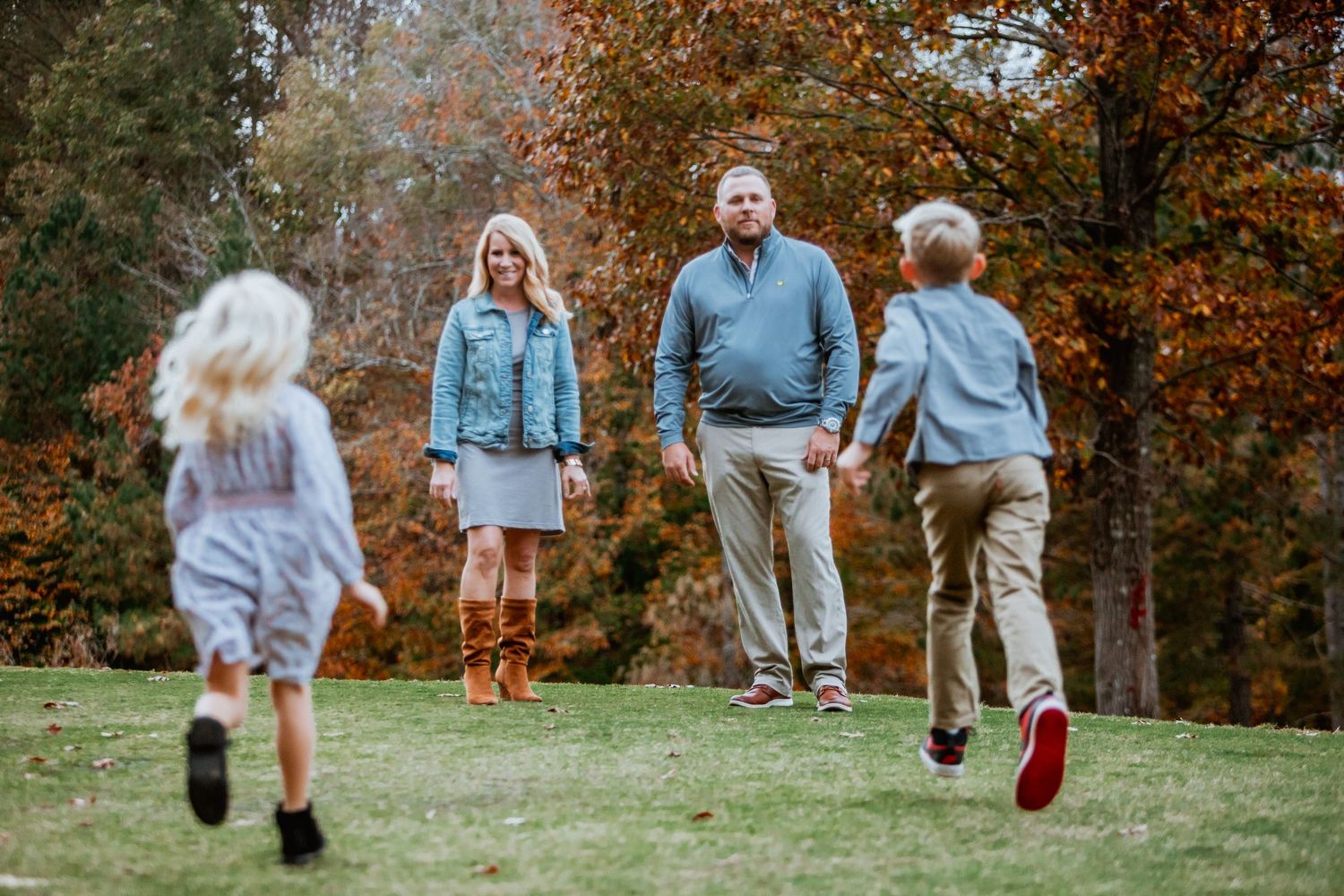 Parents watching their two children run toward them on a grassy lawn during fall family photos.