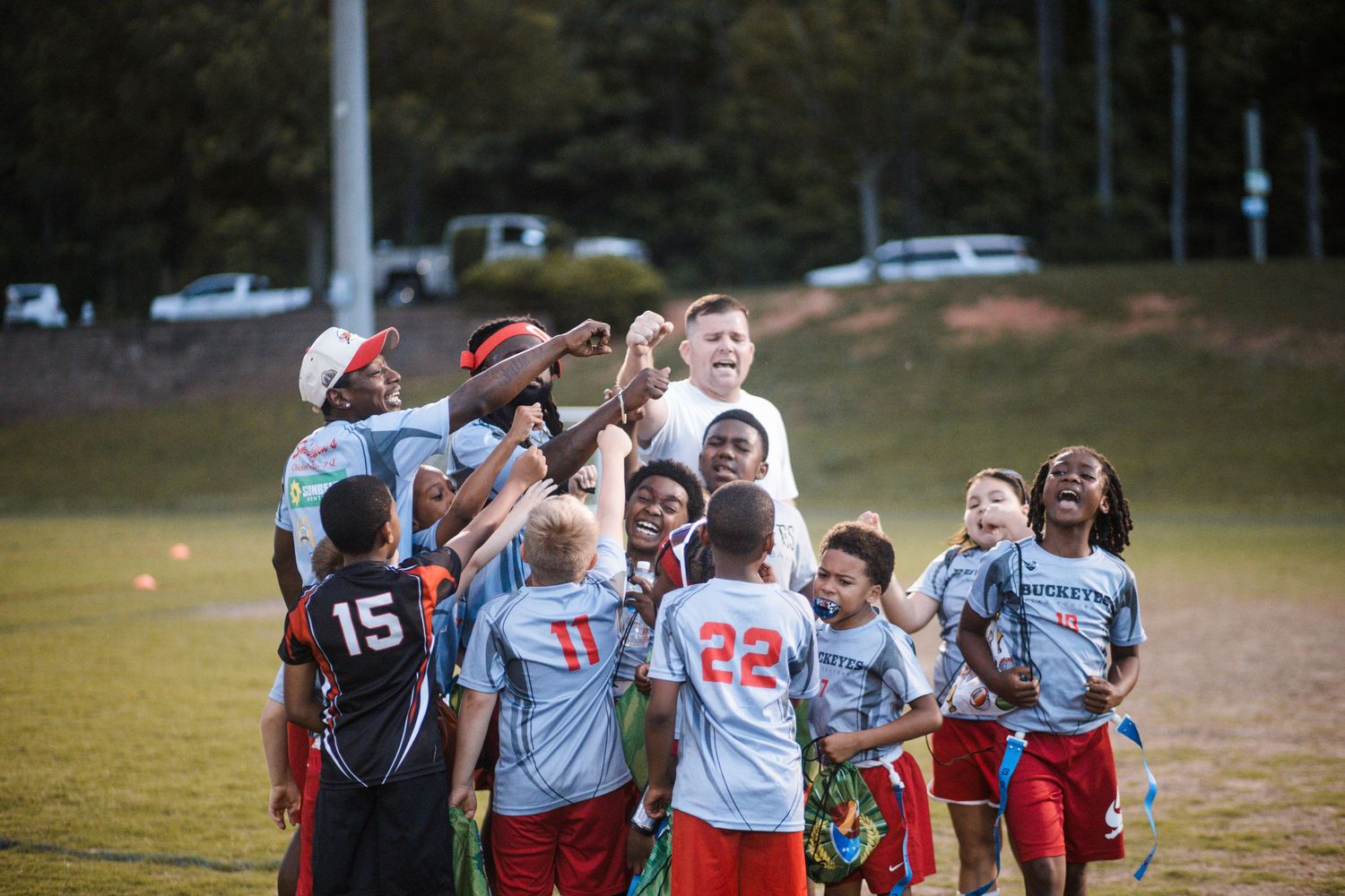 Youth flag football team huddles together celebrating on a green field during a game.