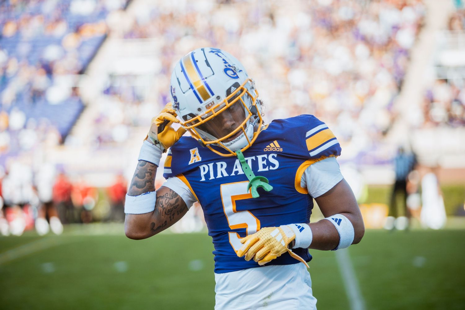 ECU Pirates football player #5 adjusts his helmet on the sideline before a game.
