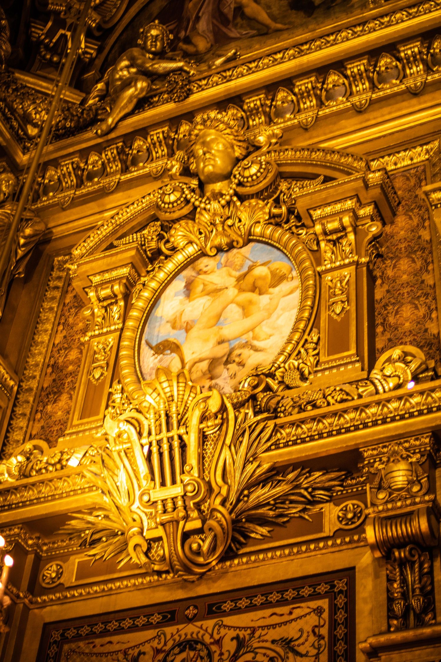 Ornate gilded baroque ceiling with a painted cherub medallion and decorative golden carvings inside a grand opera house.