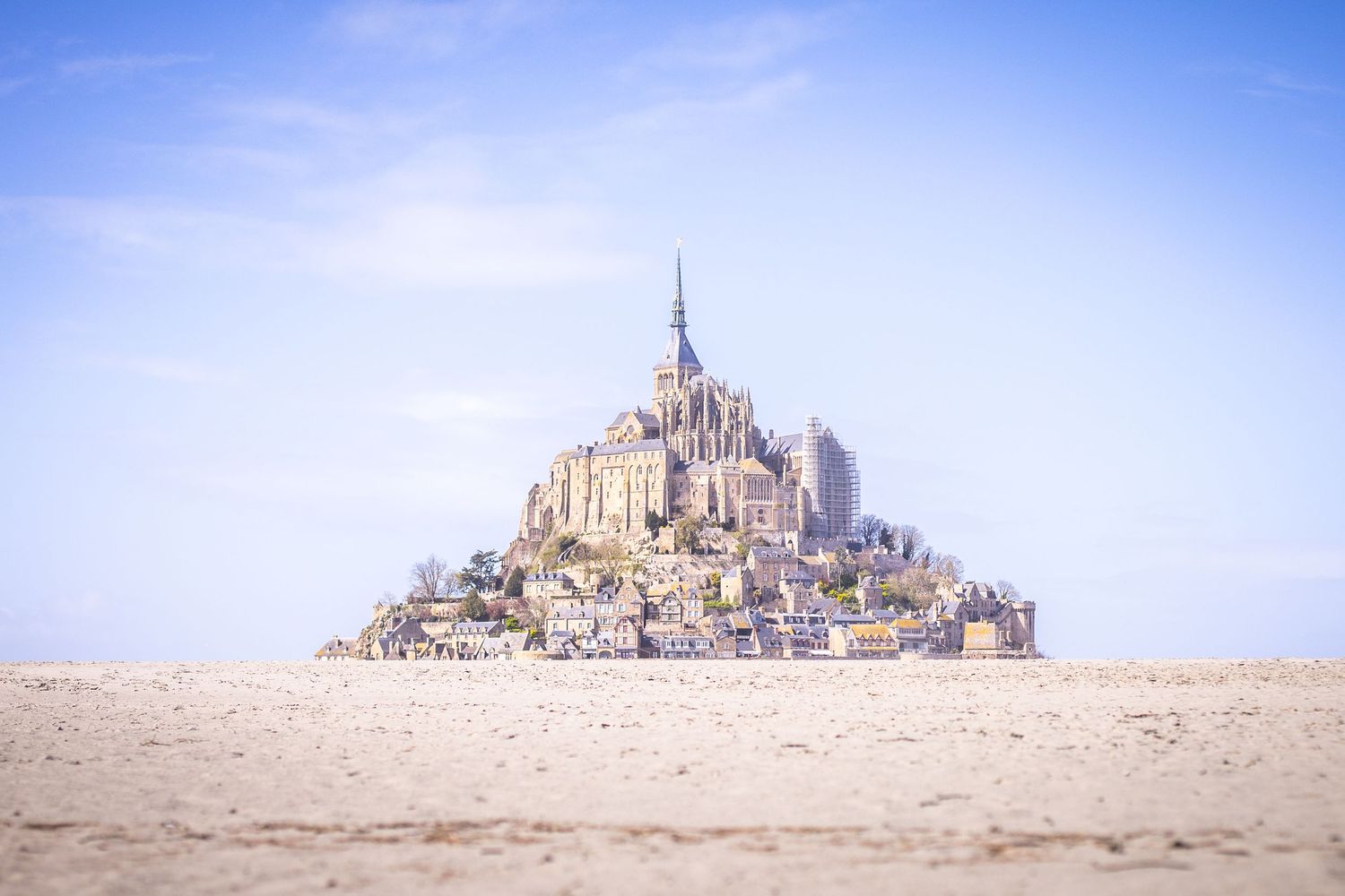 Distant view of Mont Saint-Michel medieval fortress rising above vast sandy tidal flats in France.