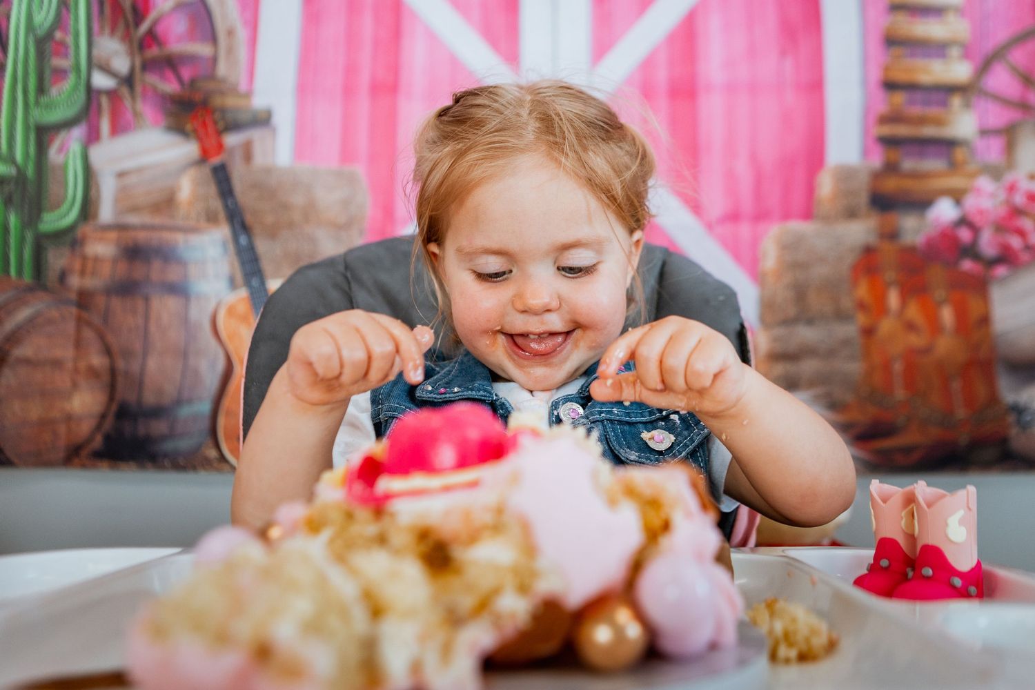 Happy toddler girl smiling while digging into a decorated cake at a birthday celebration.
