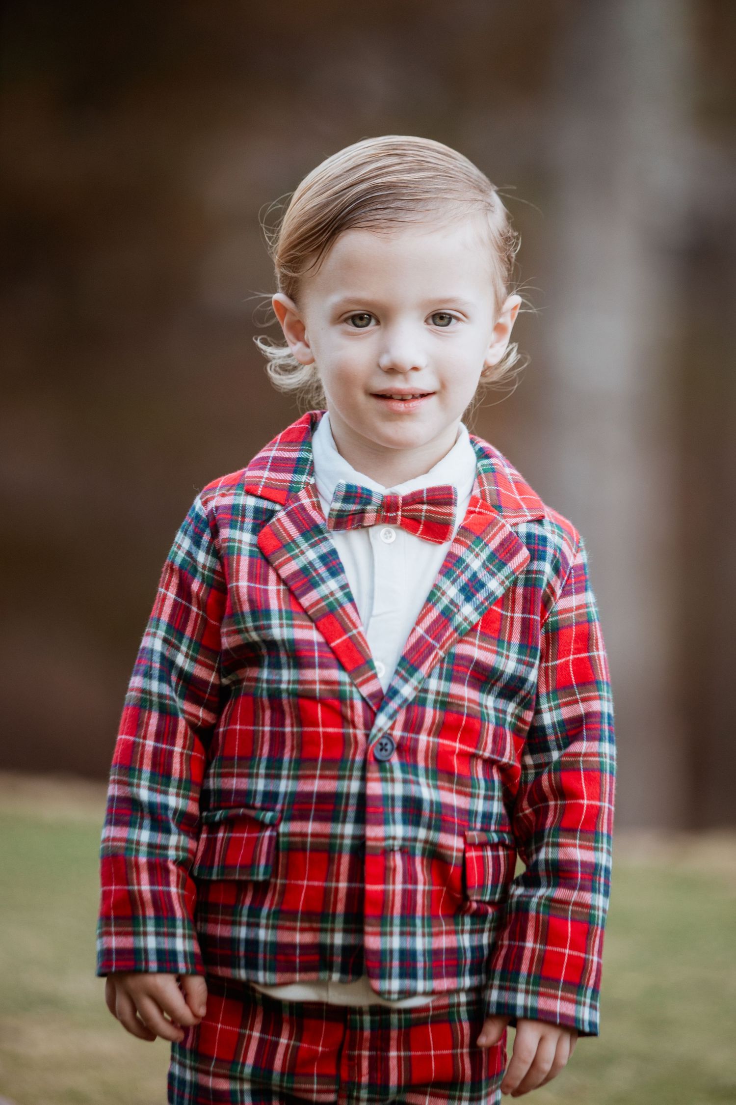 Adorable toddler in red plaid blazer and matching pants with red bow tie outdoors.
