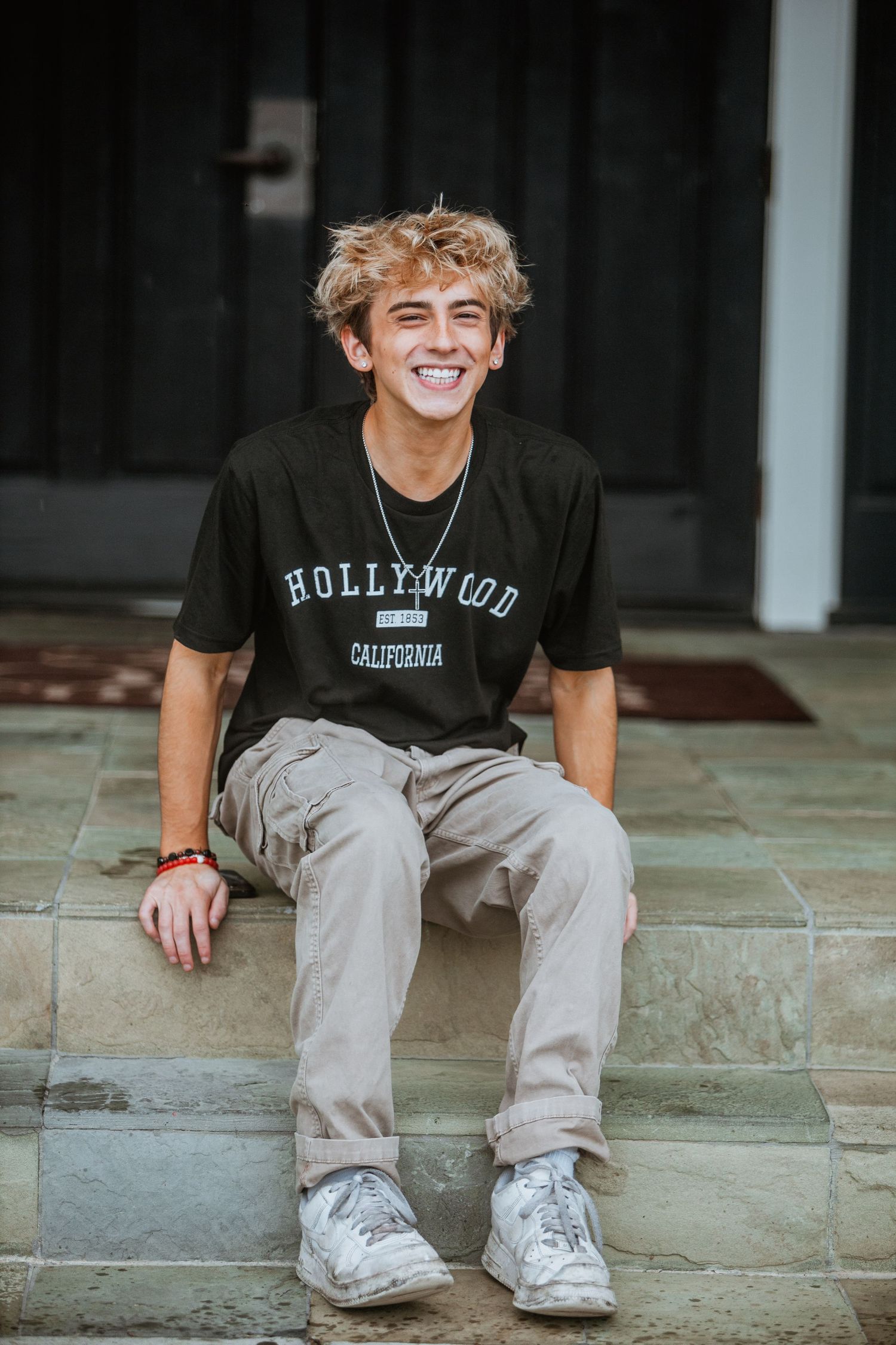 Teen boy in Hollywood California black t-shirt sitting on stone steps laughing.