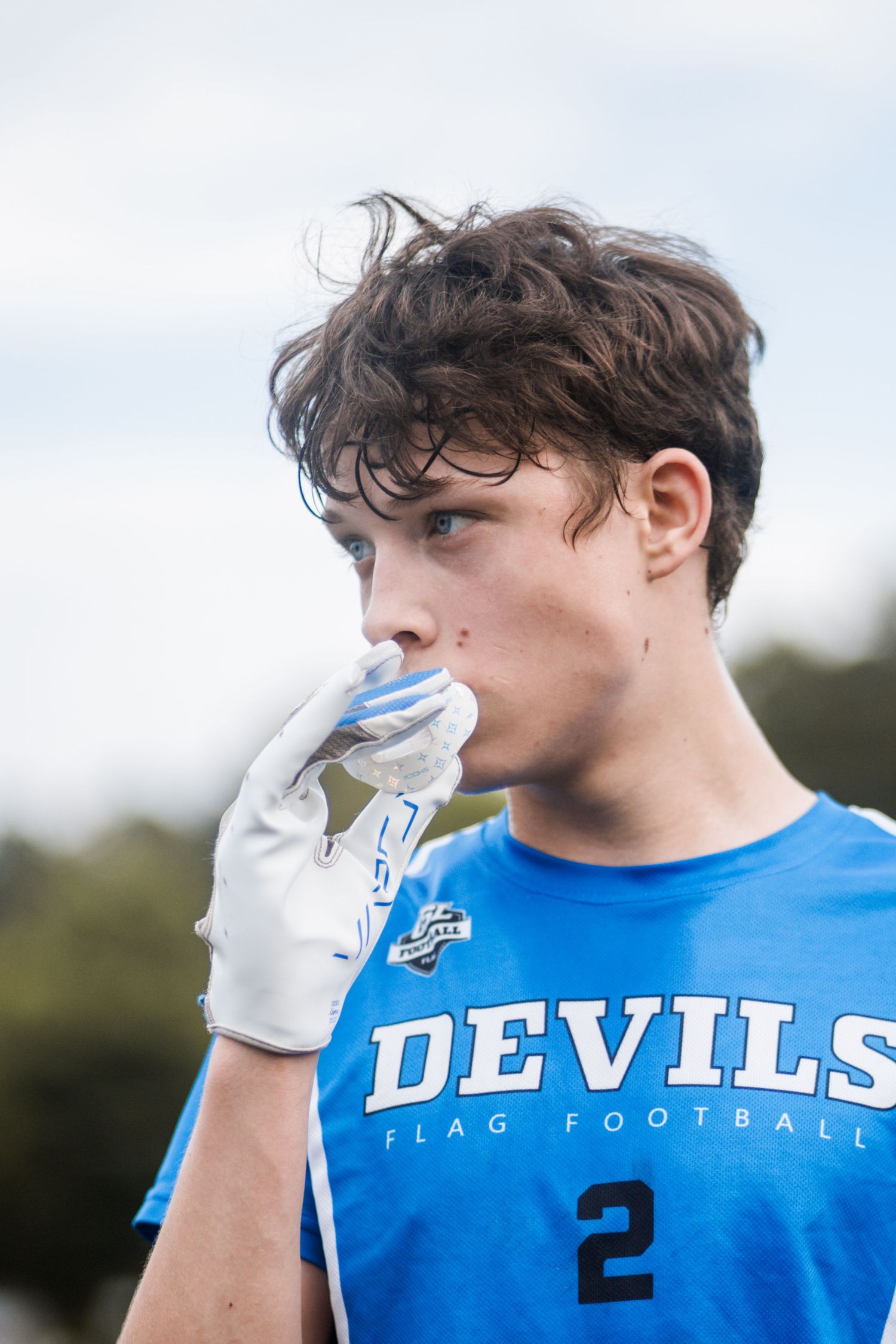 Teen boy in Devils #2 blue flag football jersey with glove near his face.