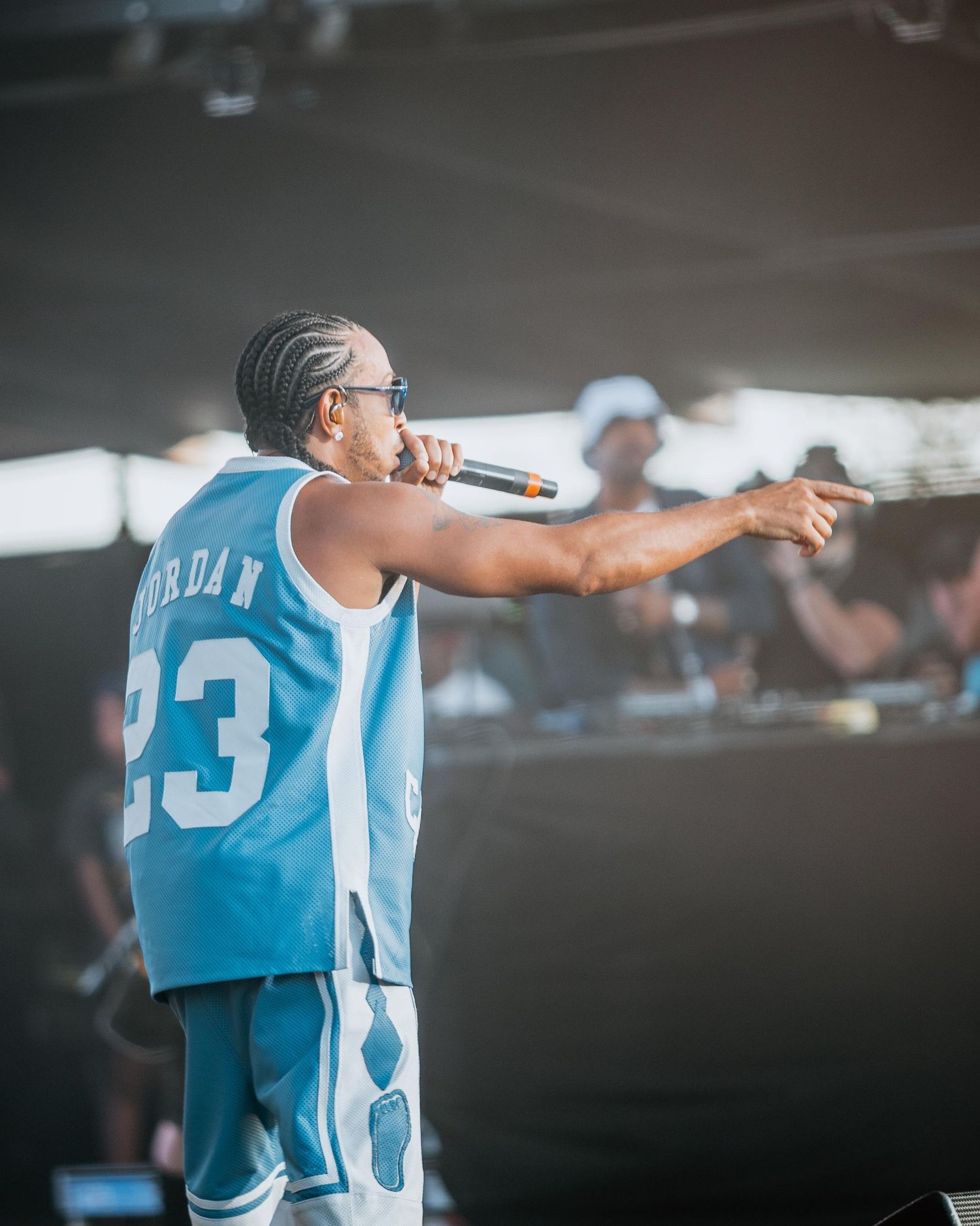 Performer in Jordan 23 jersey pointing at crowd on outdoor stage.