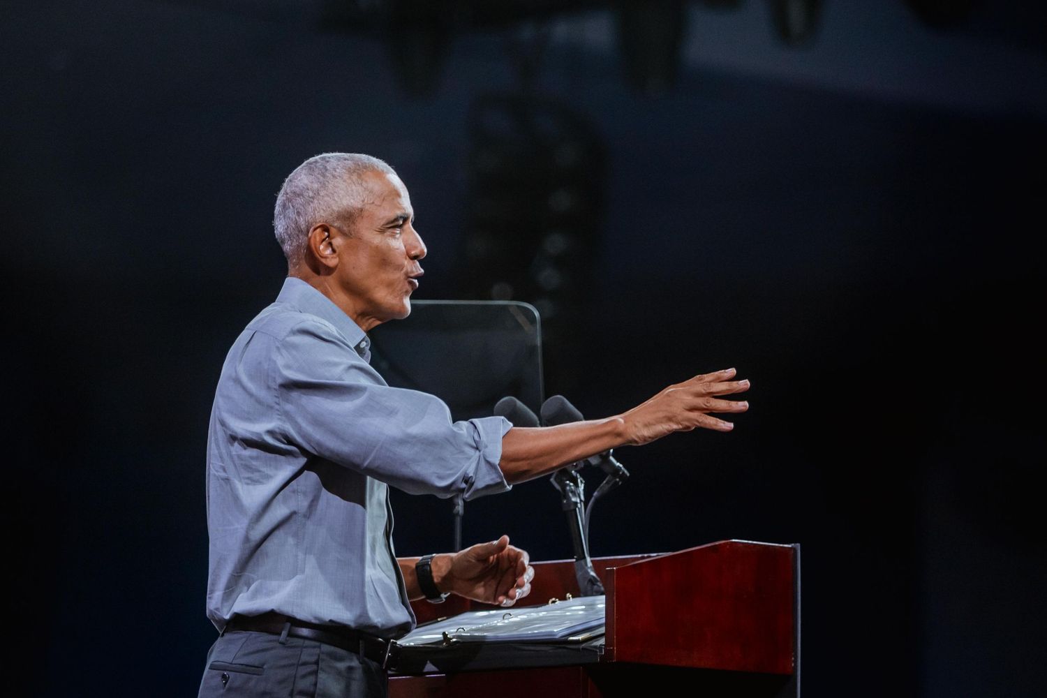 Man gesturing while speaking at a podium during a large indoor political rally.