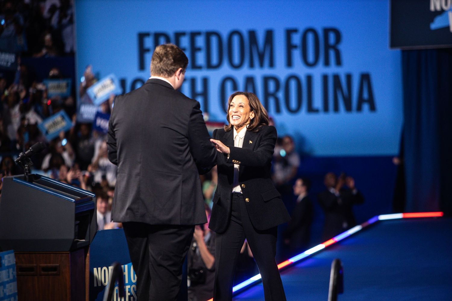 Kamala Harris shakes hands with a male speaker on stage at a Freedom for North Carolina rally.
