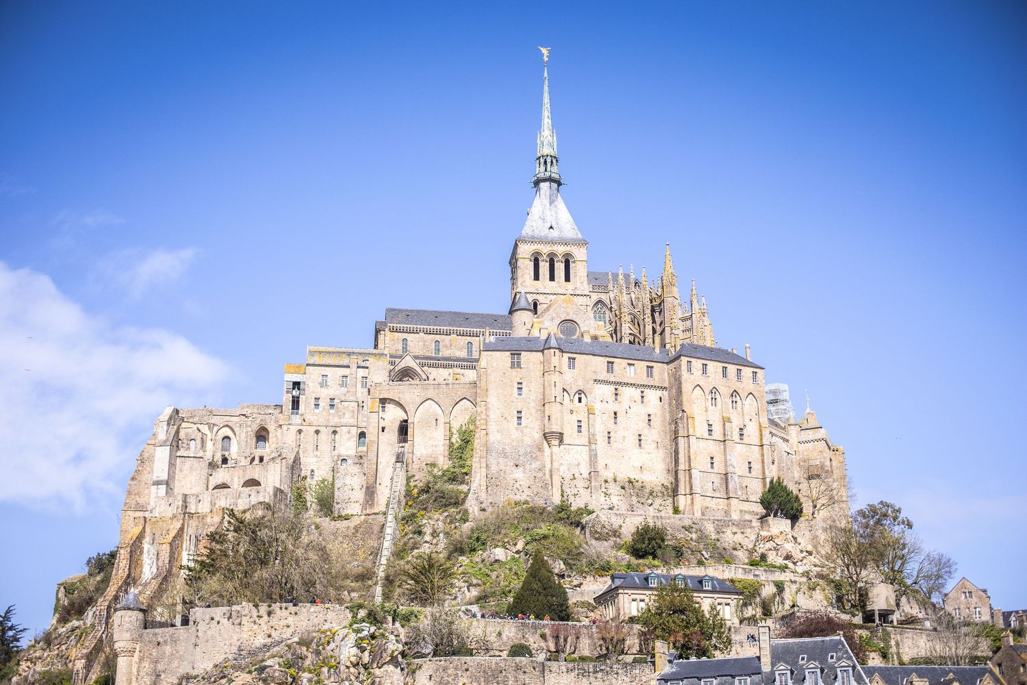 Mont Saint-Michel abbey perched dramatically on a rocky island under a bright blue sky in France.