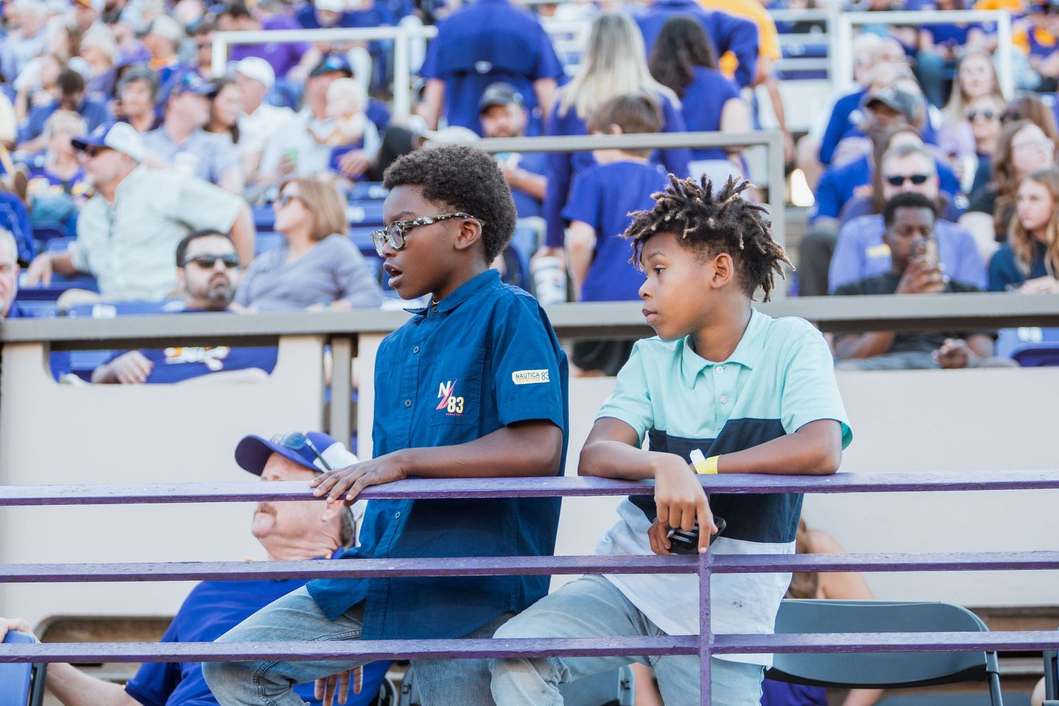 Two young boys sit in the stadium stands watching an ECU Pirates football game.