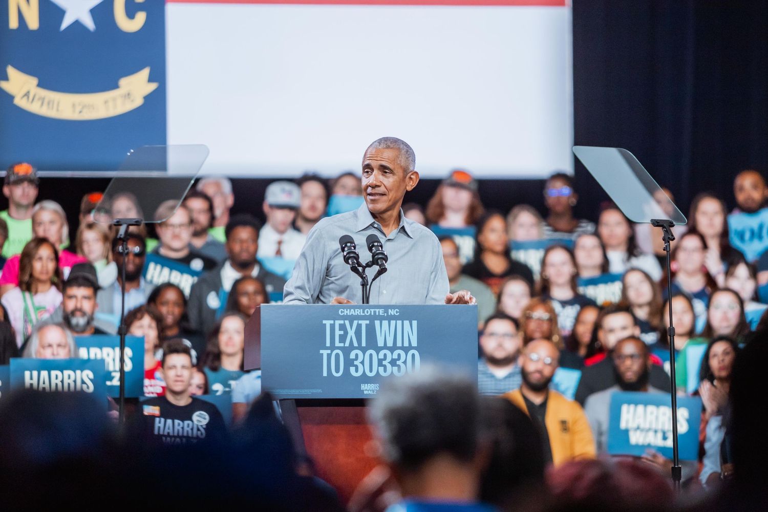 Man speaking at a Harris-Walz NC campaign rally with a large crowd holding signs.