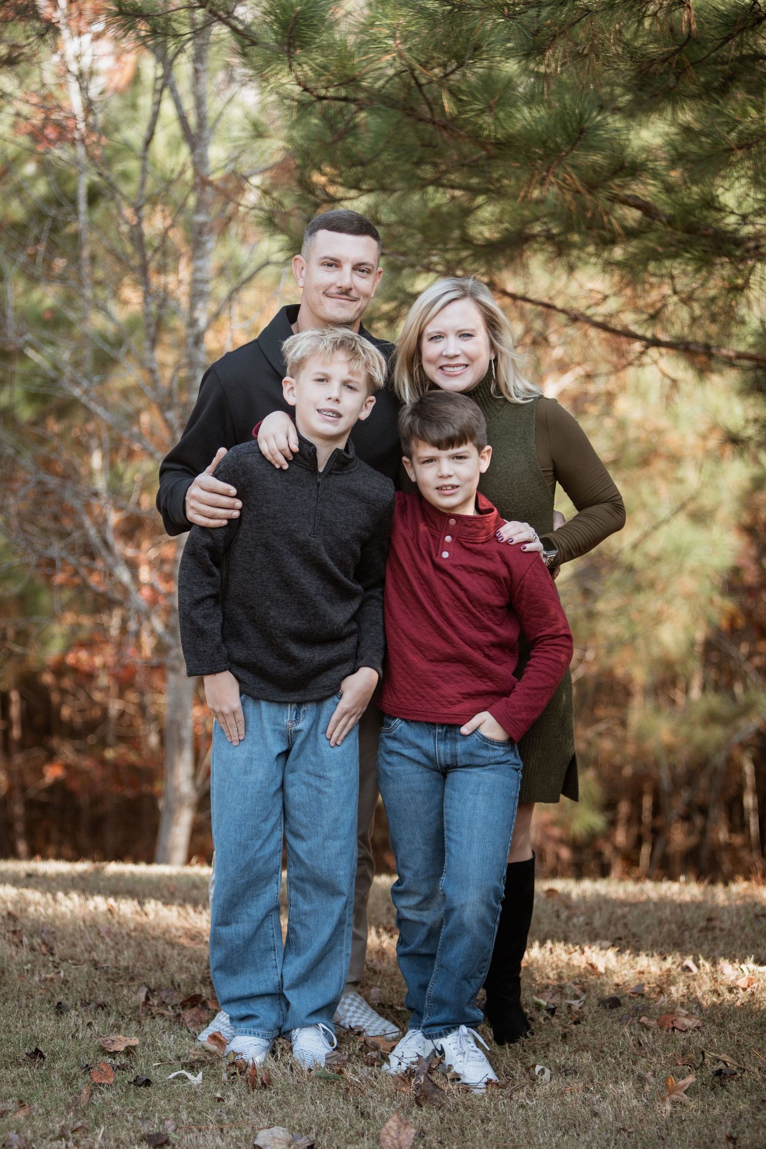 Family of four smiling together outdoors among colorful autumn trees in fall.