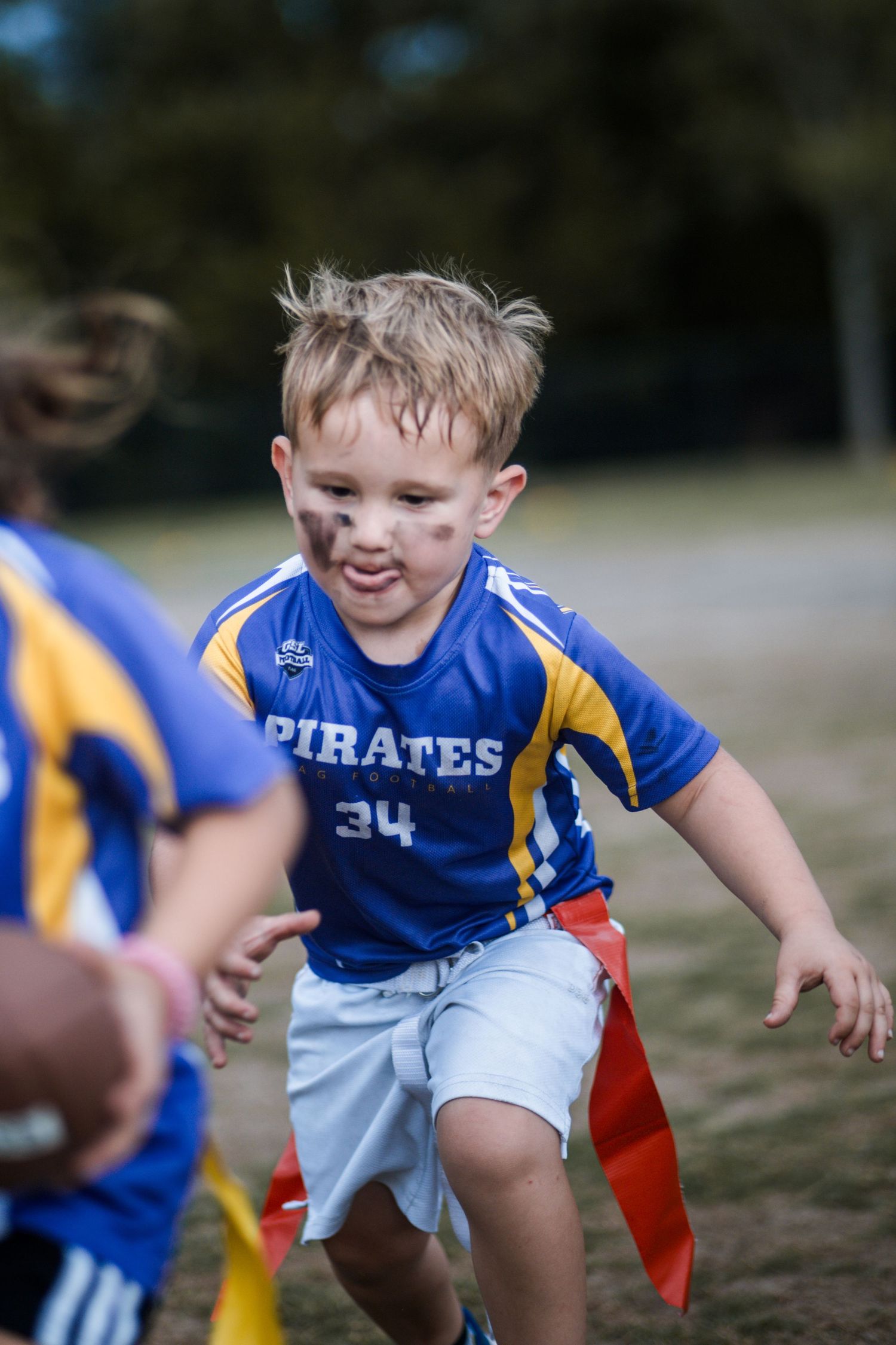 Young boy number 34 in blue Pirates jersey running with flag football flags.