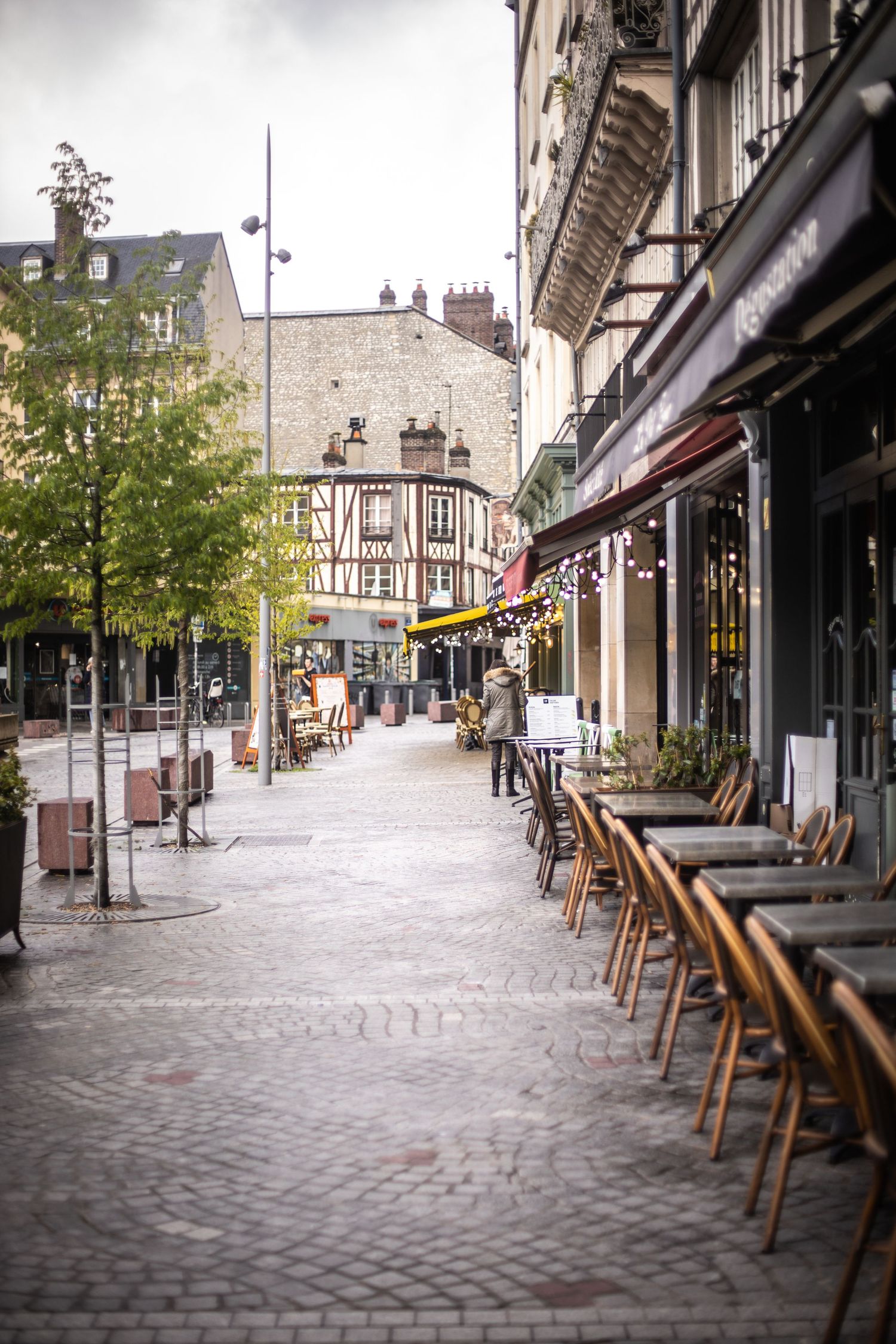 Charming cobblestone street lined with cafe chairs and historic half-timbered buildings in a French town.