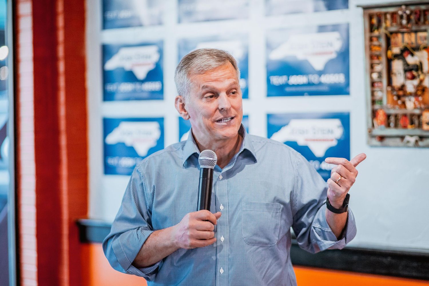 Man in blue shirt speaking into microphone at North Carolina political campaign event.