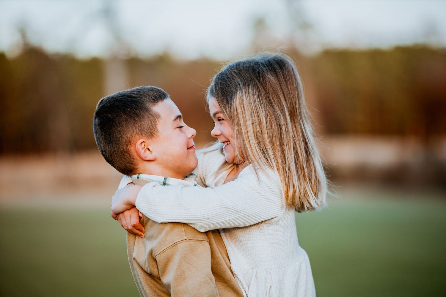 Two children smiling and hugging each other outdoors in natural light.