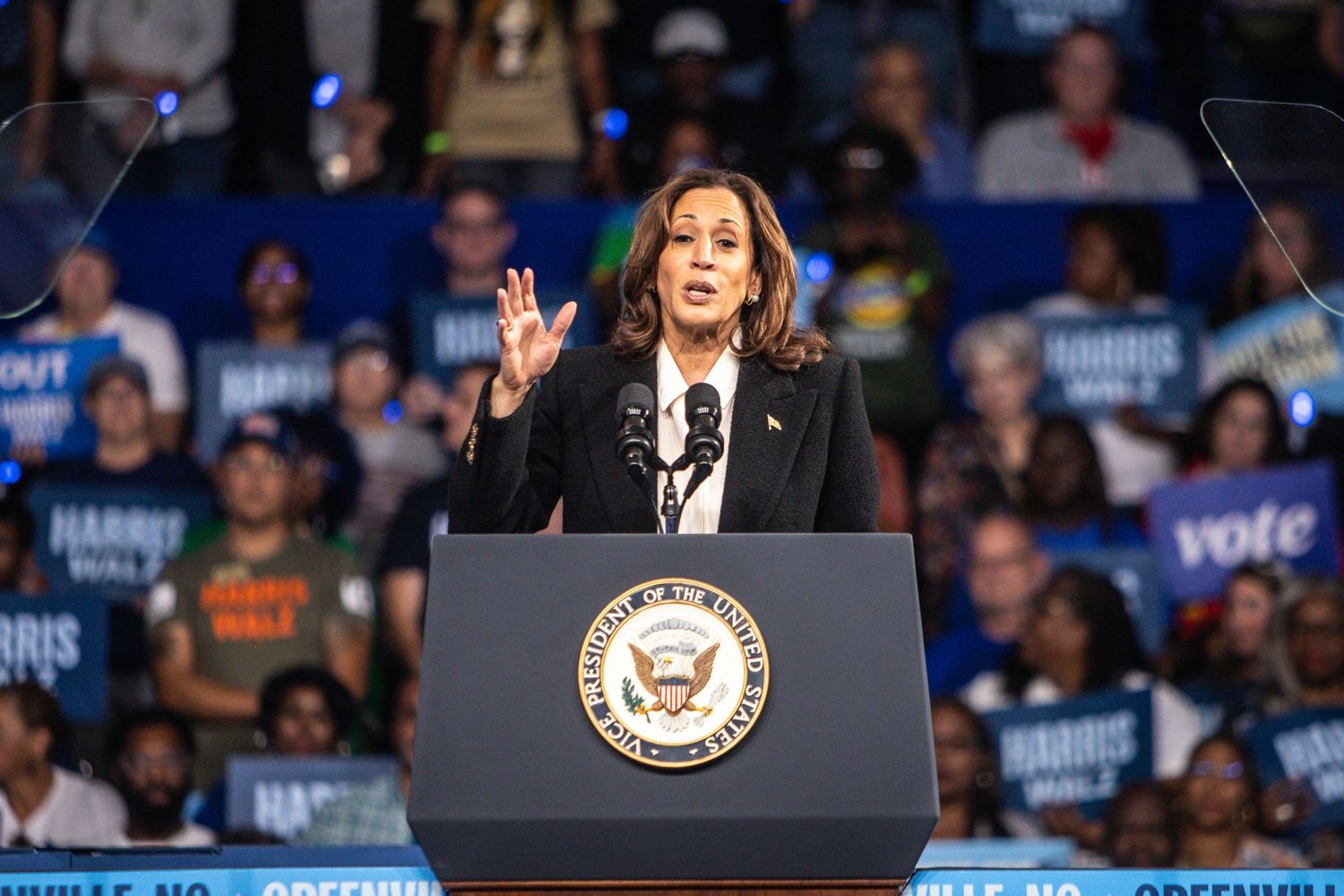 Kamala Harris speaks at a podium before a large crowd at a Harris-Walz campaign rally.