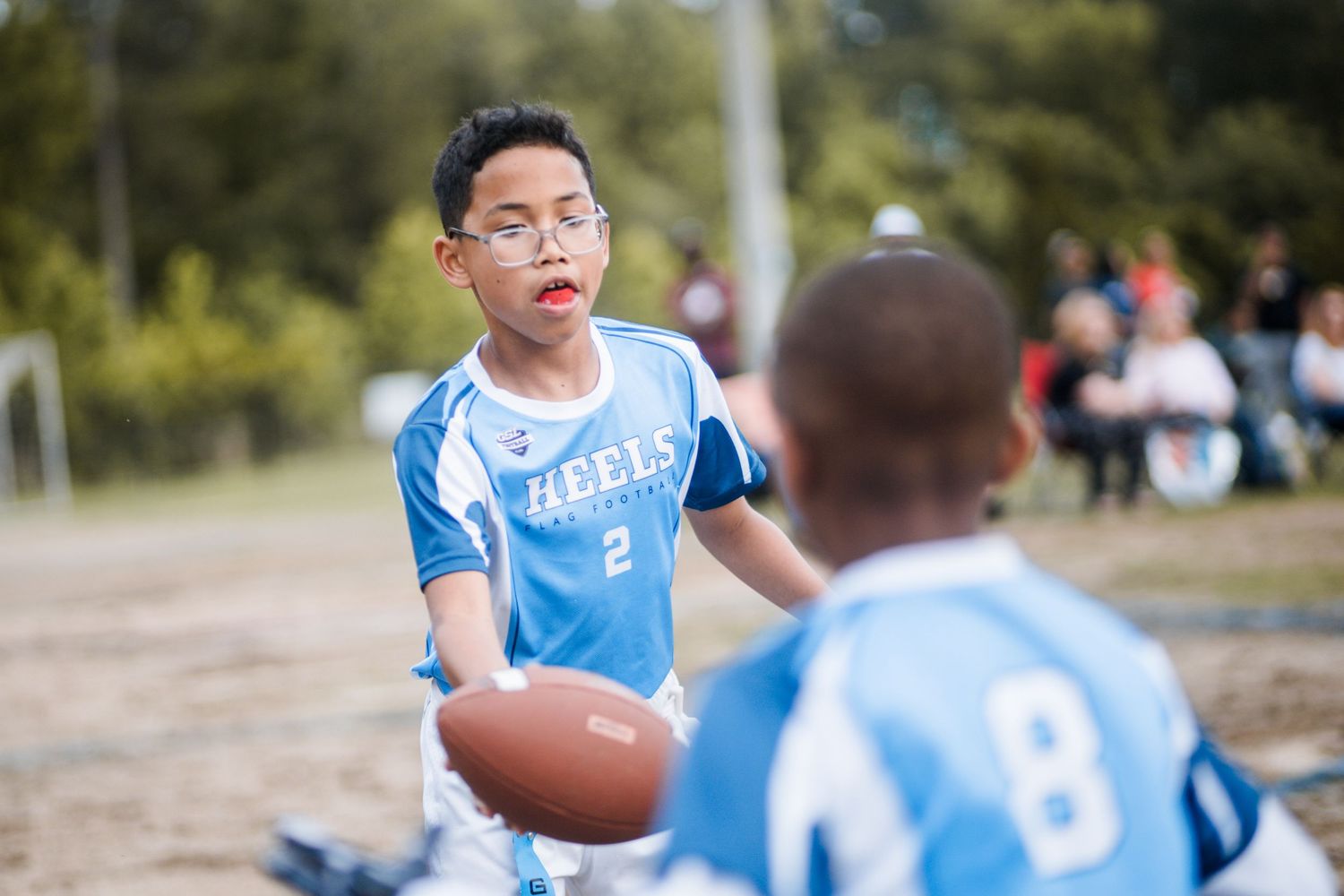 Young boy in Heels #2 jersey passing football to teammate during flag football game.