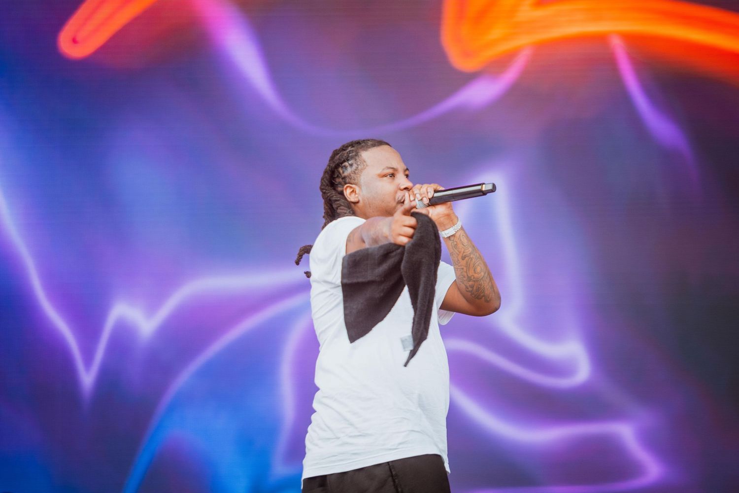 Male artist performing on stage with purple and blue neon light backdrop.