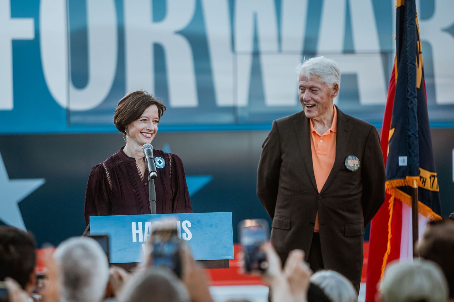 Two people smile together at Harris 2024 Forward campaign rally podium.