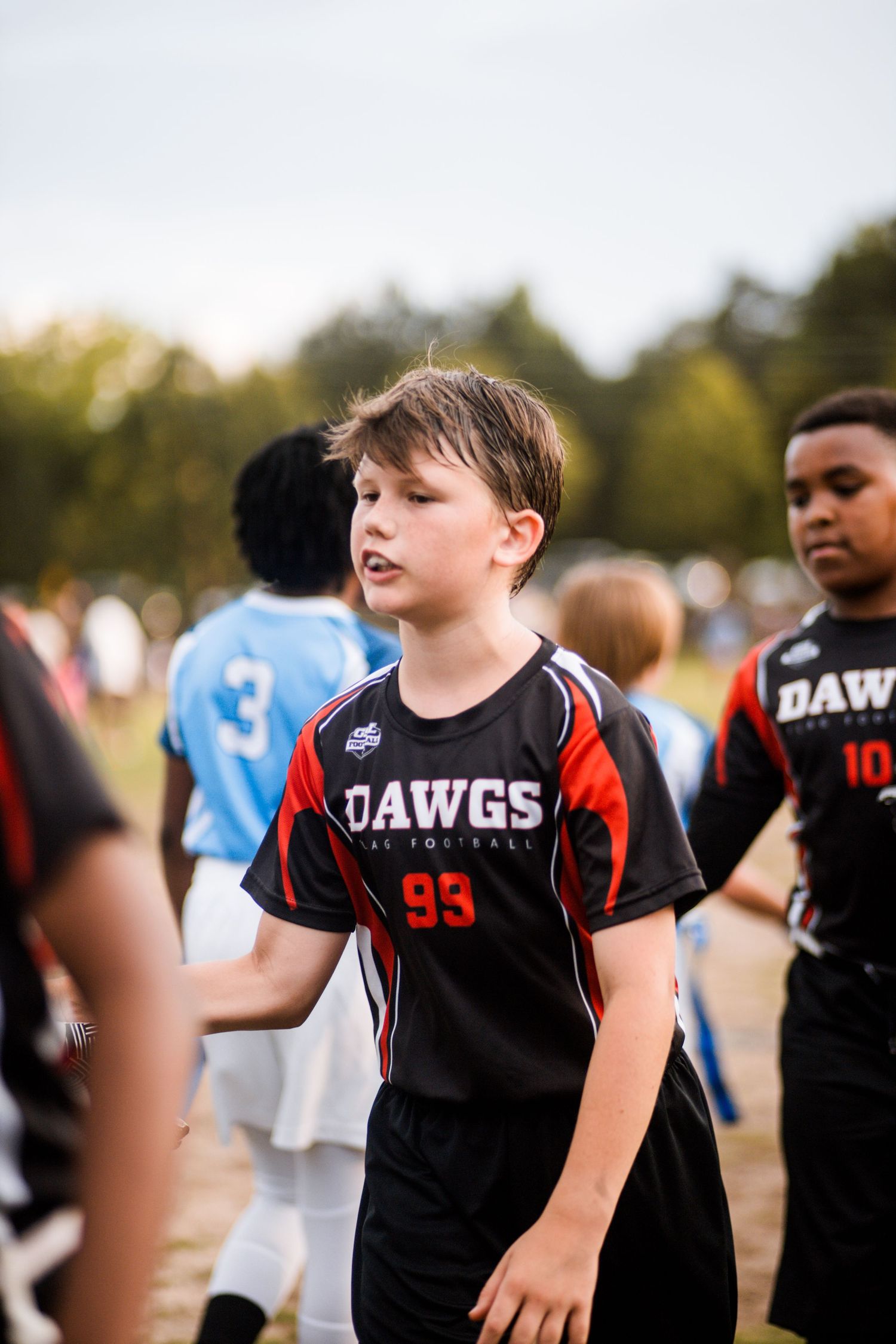 Young boy in Dawgs #95 black flag football jersey walking on outdoor field.