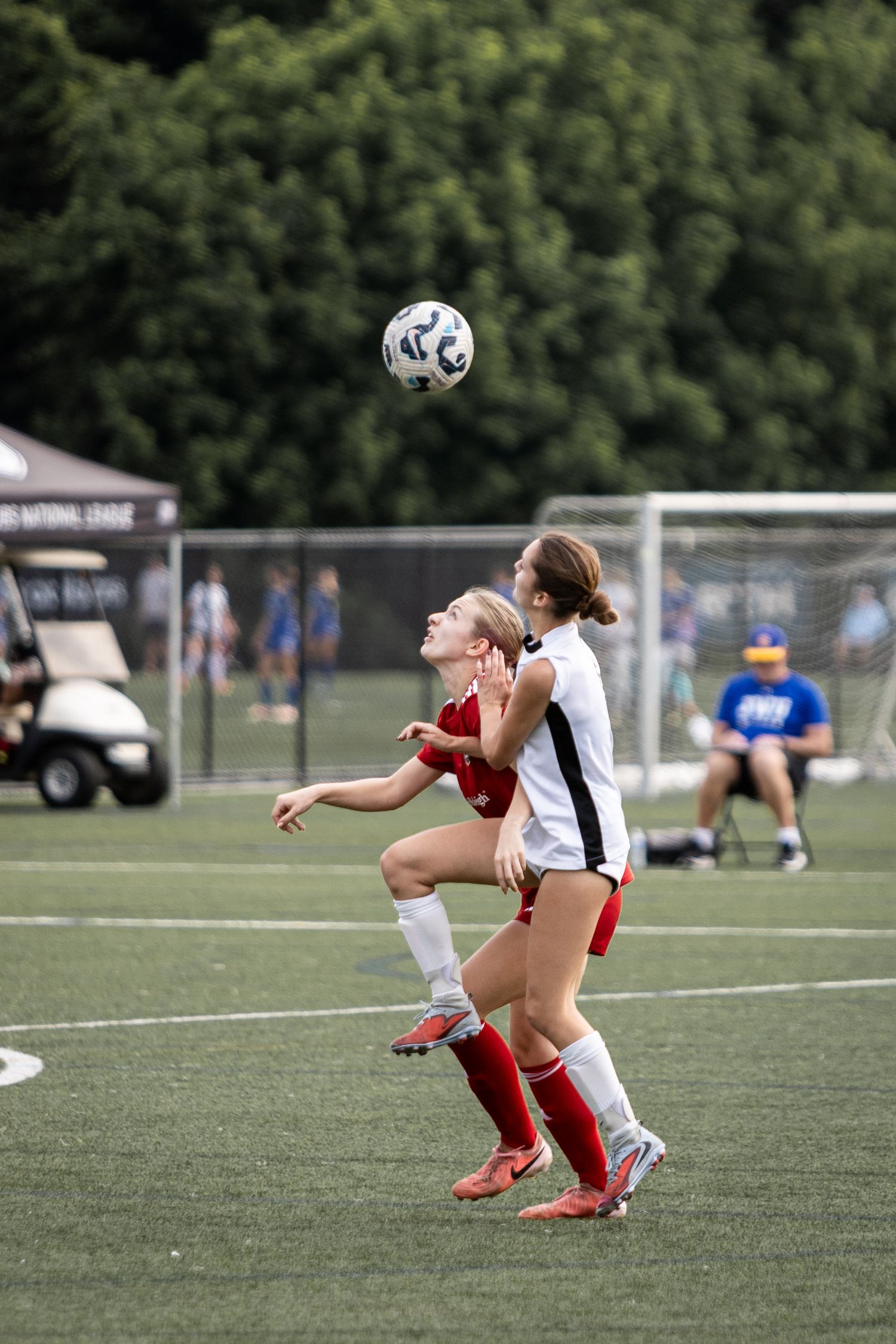 Two female soccer players jump to head the ball during an intense youth soccer match outdoors.