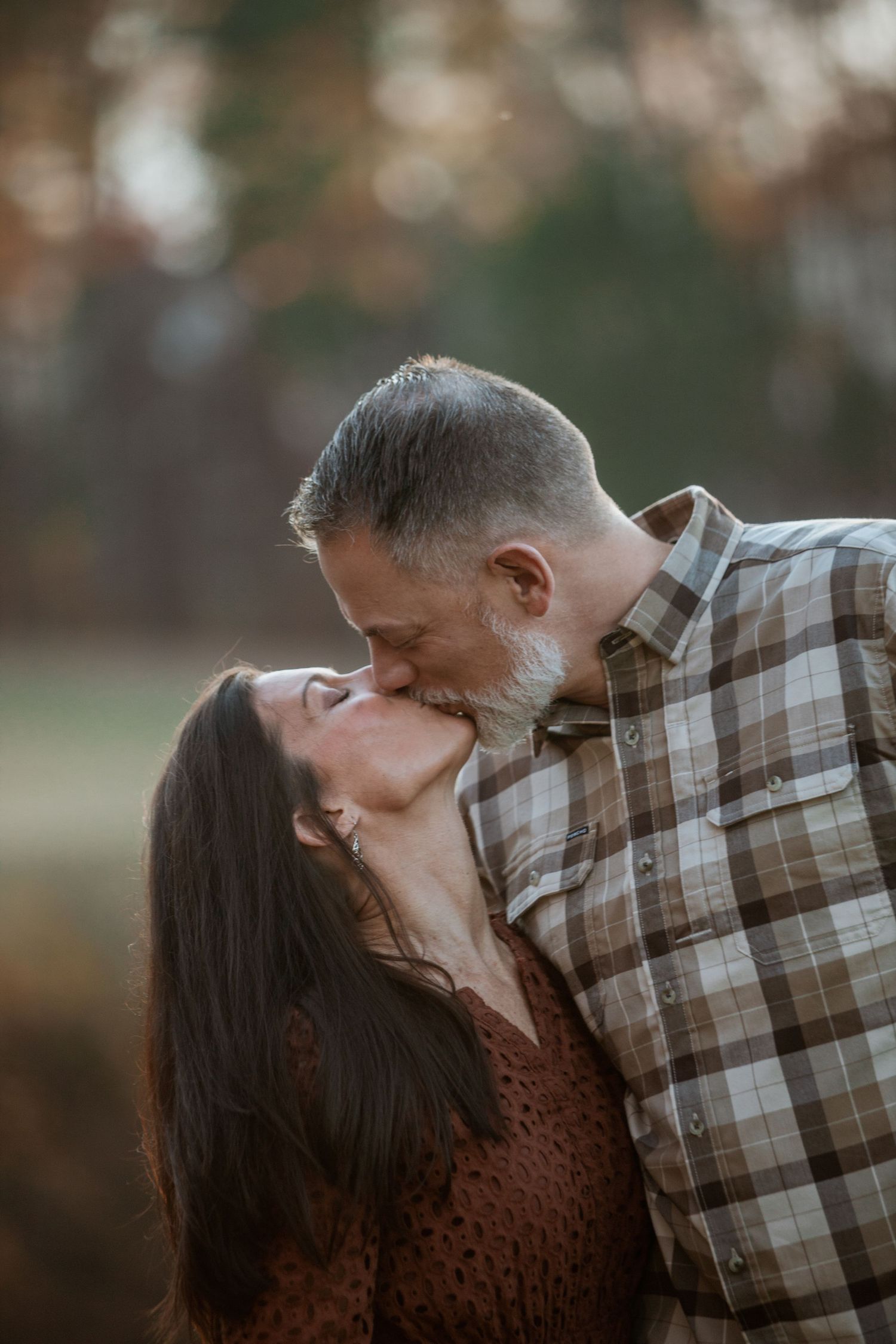 Couple sharing a tender kiss outdoors in soft autumn bokeh light.