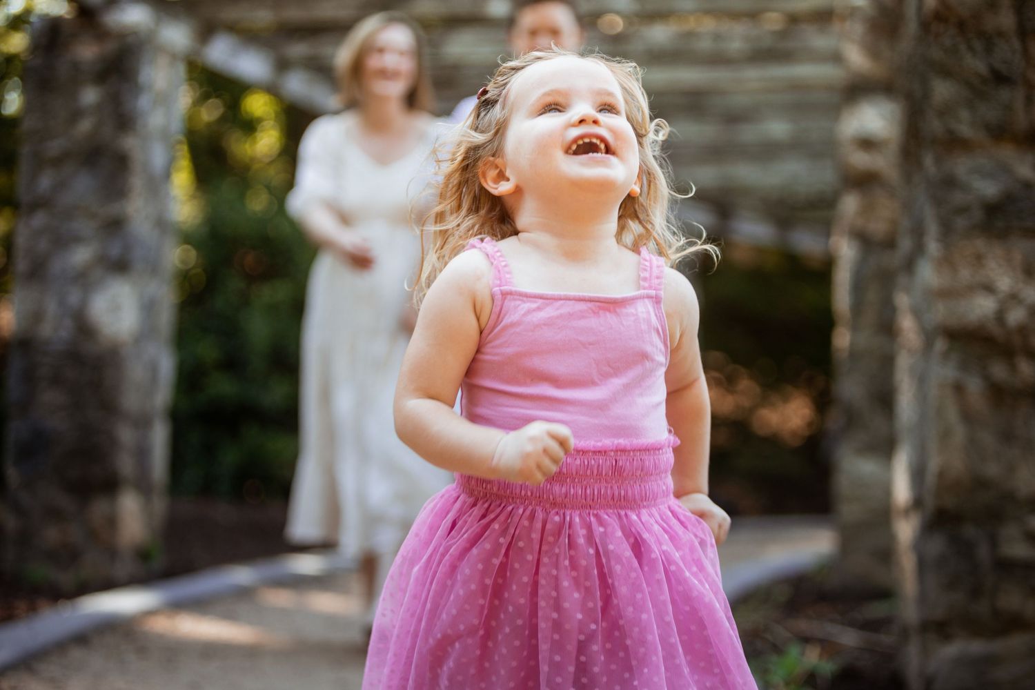 Joyful toddler girl in pink tutu dress laughing and playing outdoors in a garden.