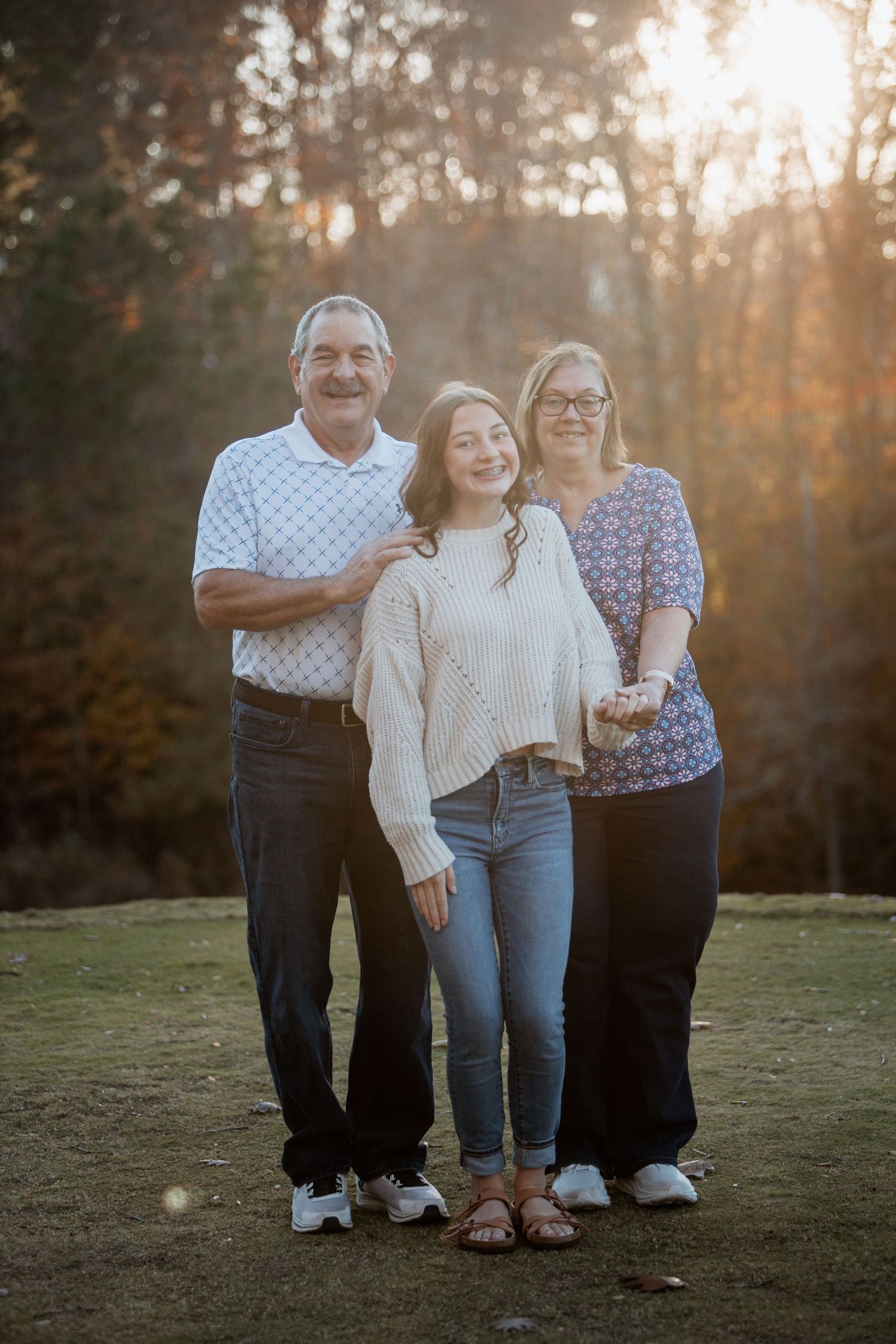 Grandparents posing with their granddaughter in a warm golden-hour outdoor fall family portrait.