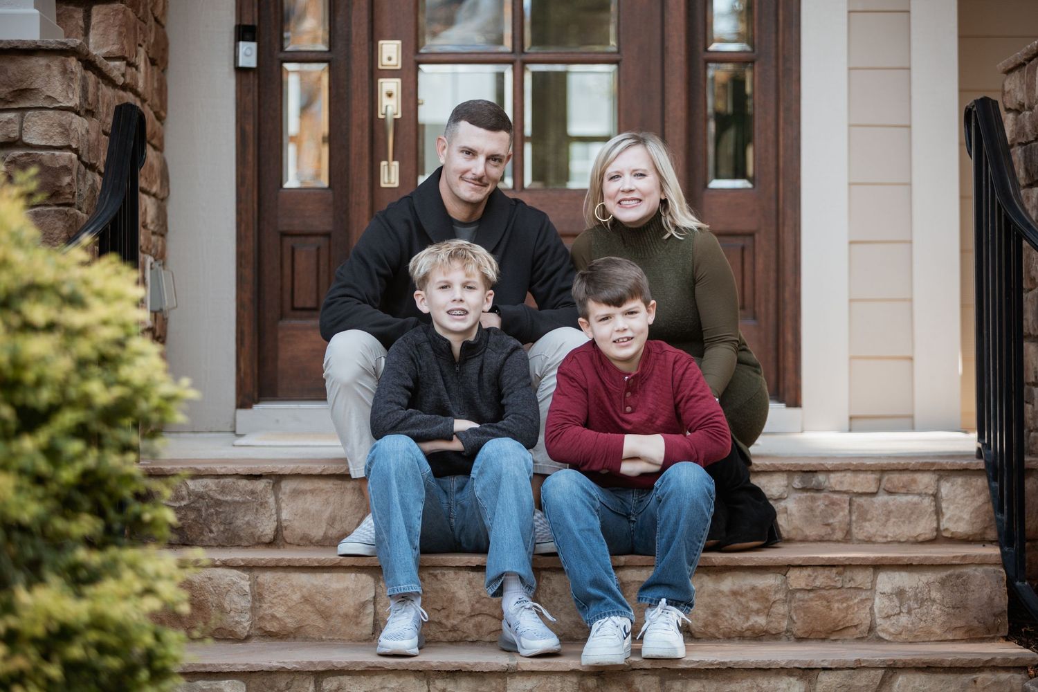 Family of four sitting together on stone front porch steps of a home in fall.