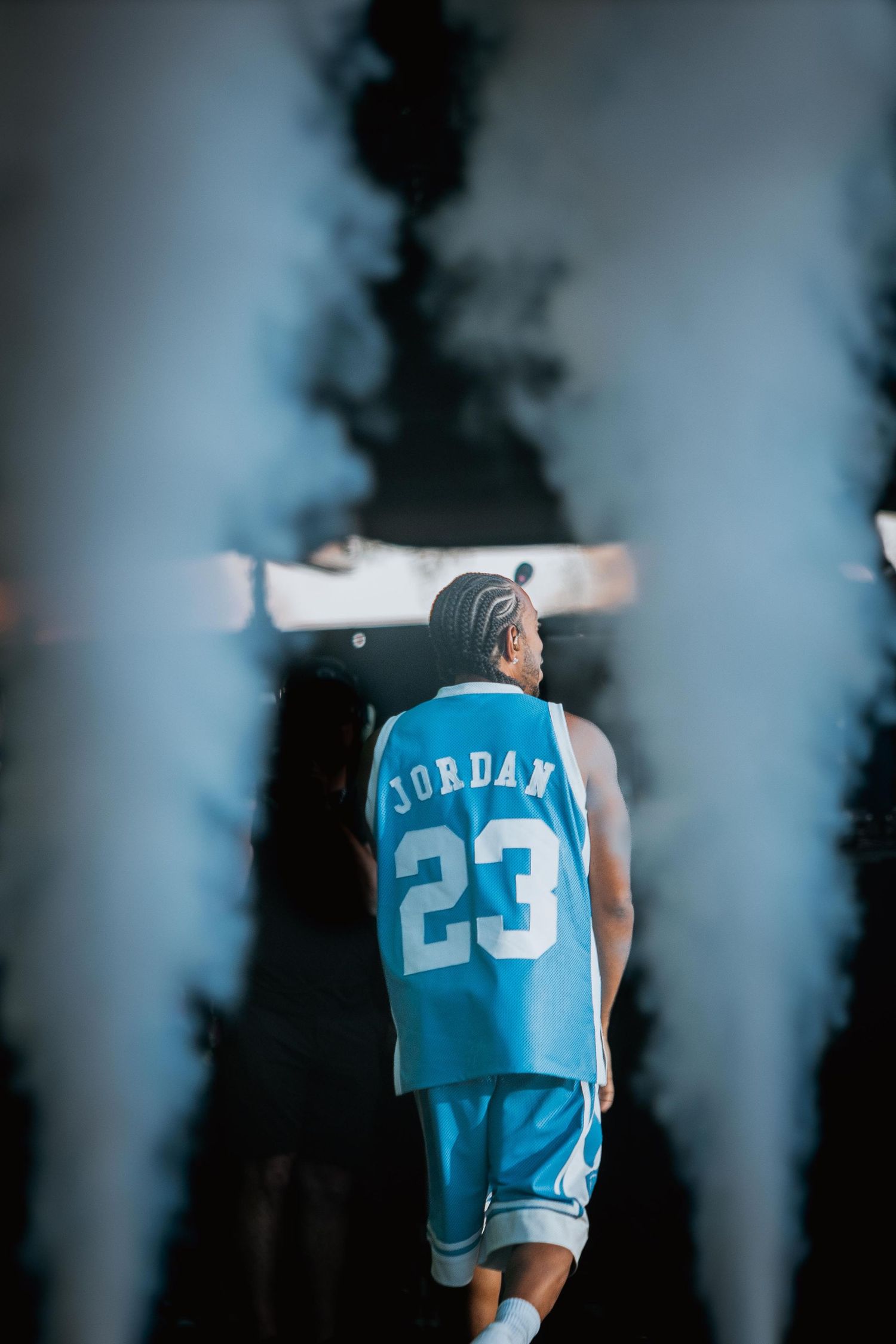Performer in Jordan 23 jersey walking through smoke on outdoor stage.