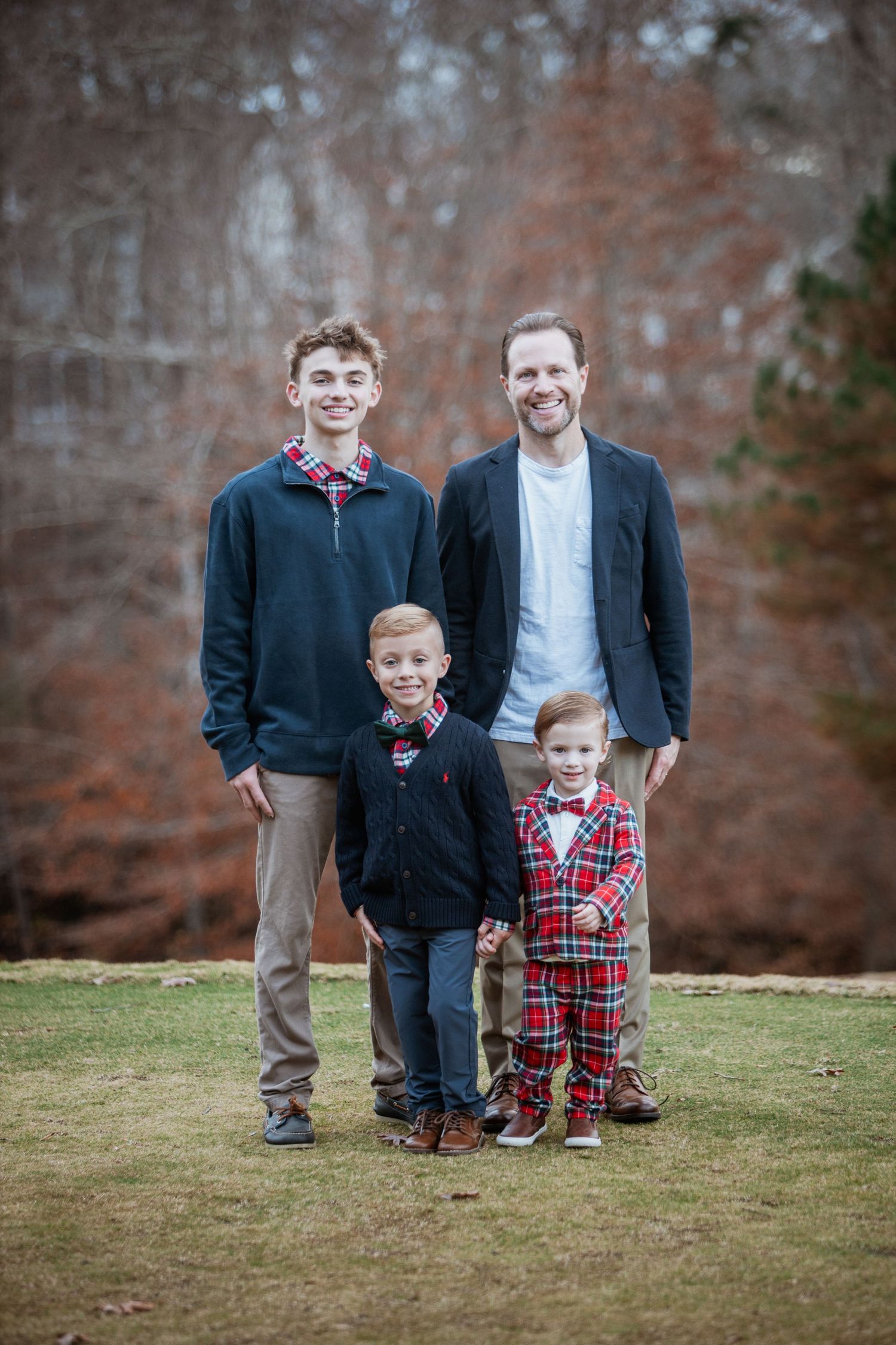 Family portrait of father and three sons in coordinating outfits posing outdoors.