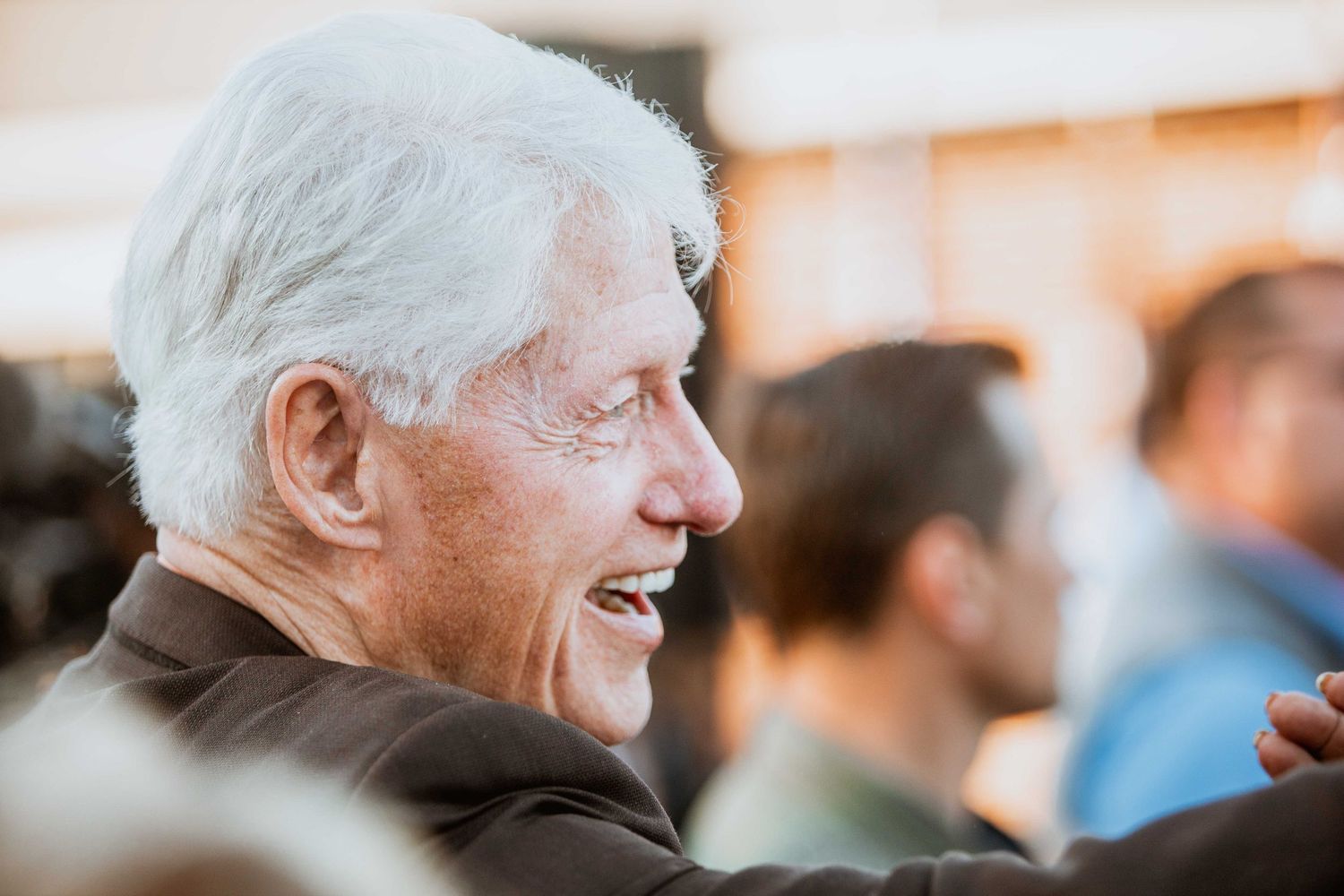 Elderly white-haired man laughing joyfully in profile at an outdoor social gathering event.