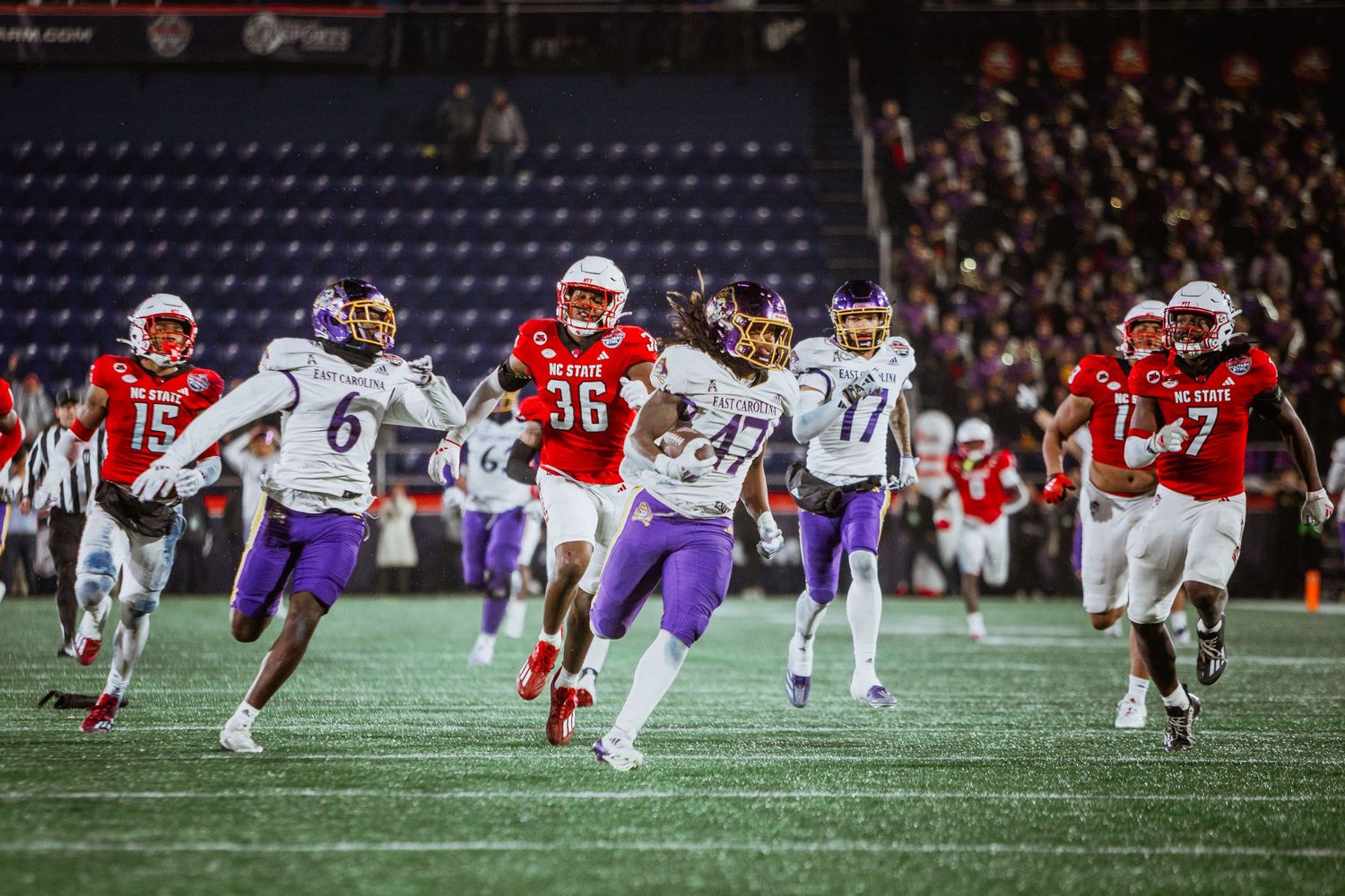 ECU Pirates football player #36 runs with the ball during a night game against a team in purple uniforms.