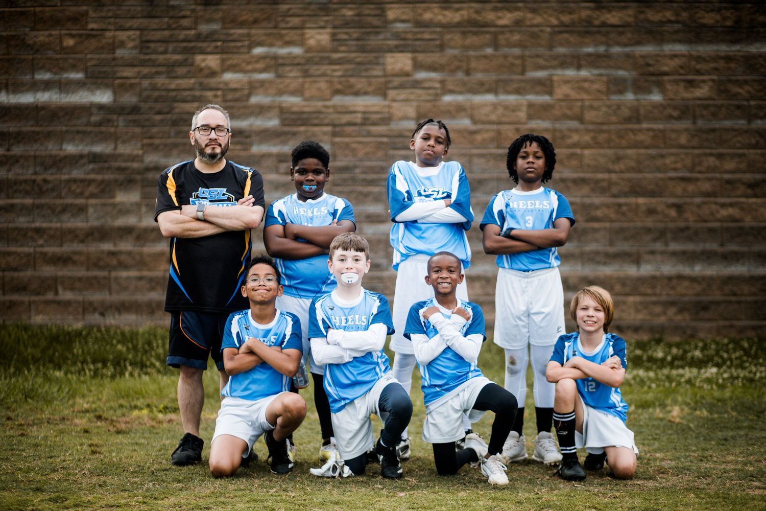 Youth flag football team in blue jerseys poses with coach for small group team photo outdoors.