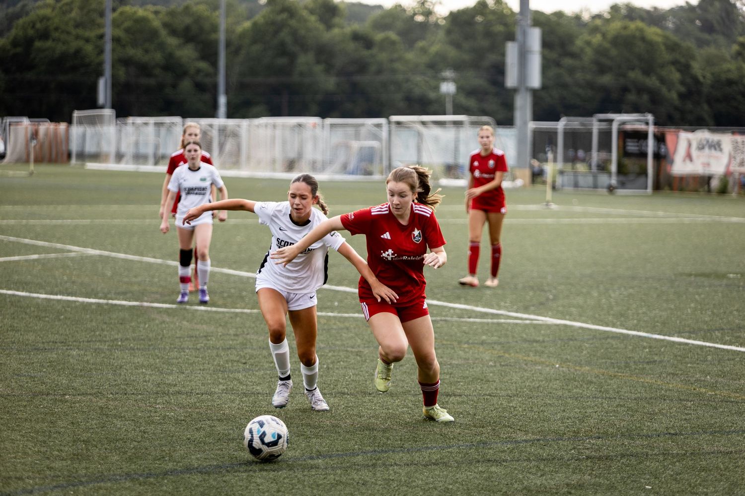 Two female soccer players battle for possession during competitive womens soccer match on turf field.