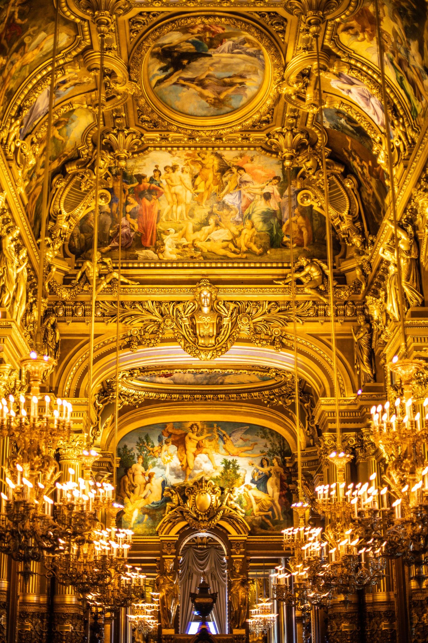 Lavishly decorated golden ceiling with baroque frescoes and glowing chandeliers inside the Paris Opera Garnier.