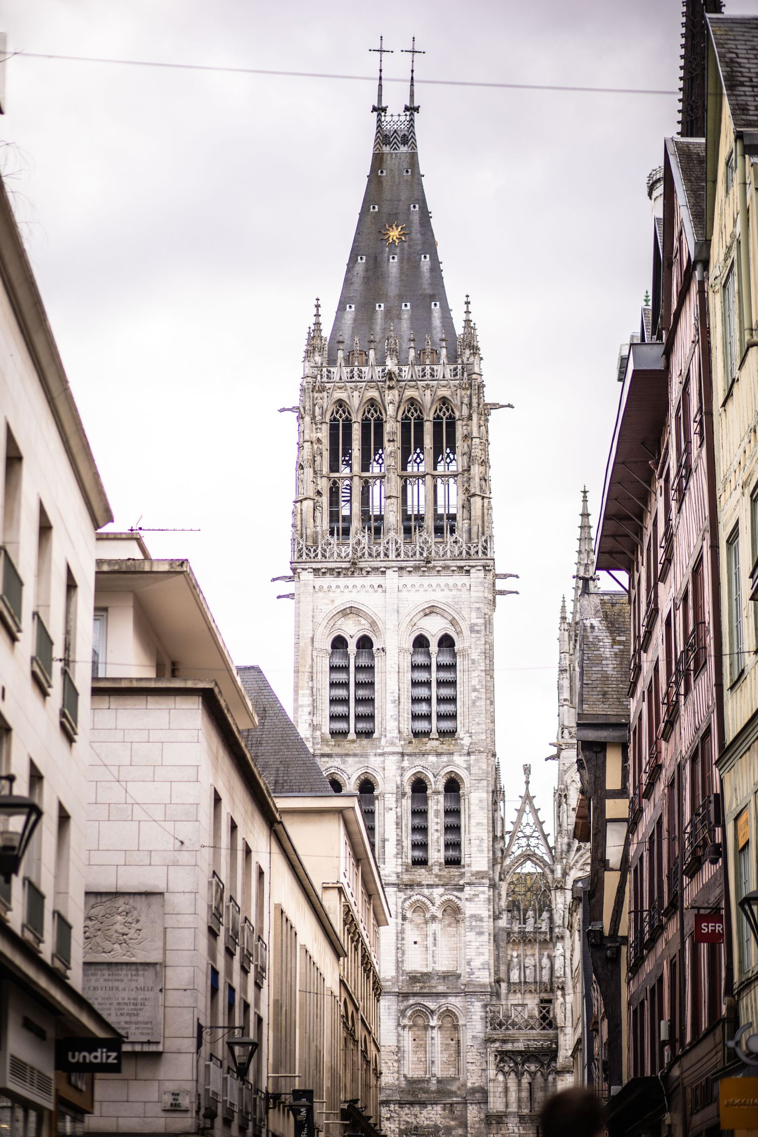 Gothic spire of Rouen Cathedral rising above narrow historic streets in Normandy, France.