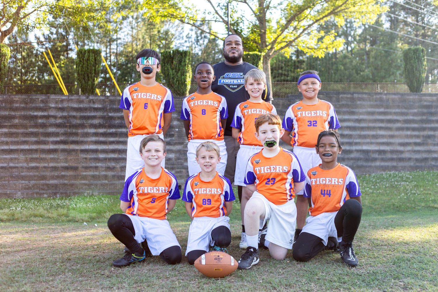 Youth flag football team in orange Tigers jerseys poses with coach for team photo on grass.