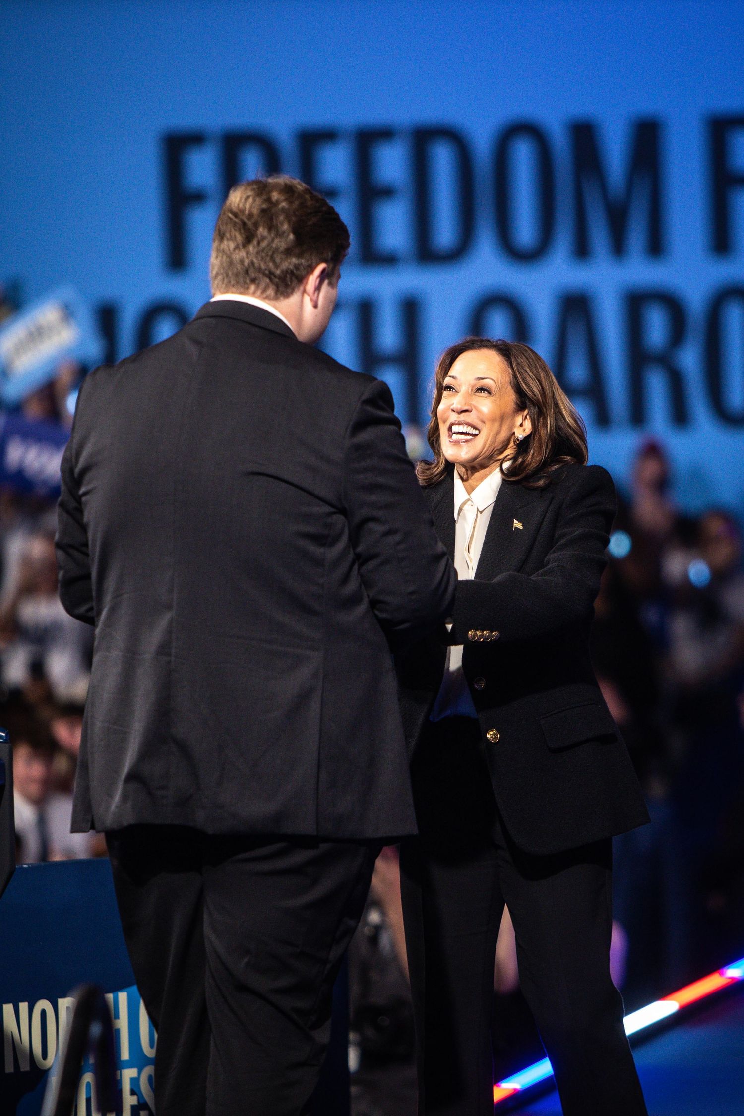 A woman in a black blazer smiles warmly while greeting a man in a suit at a Freedom Rally in North Carolina.