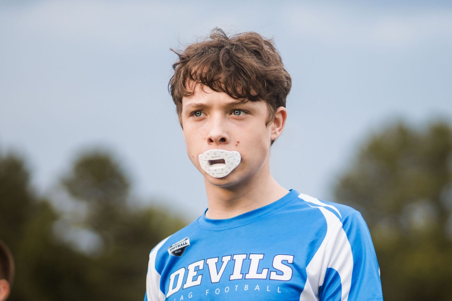 Young boy in blue Devils flag football jersey with mouthguard on sports field.