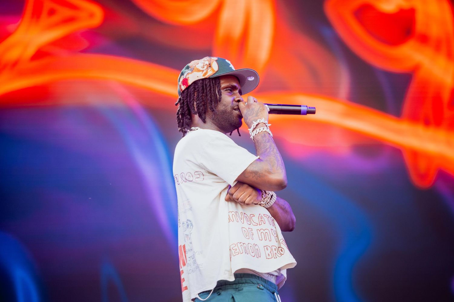 Rapper performing on stage holding microphone with colorful neon light background.