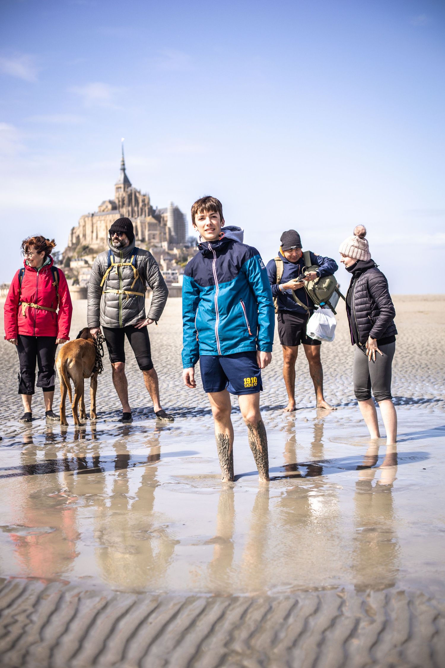 Group of tourists and a dog walking on the tidal flats near Mont Saint-Michel abbey in Normandy.