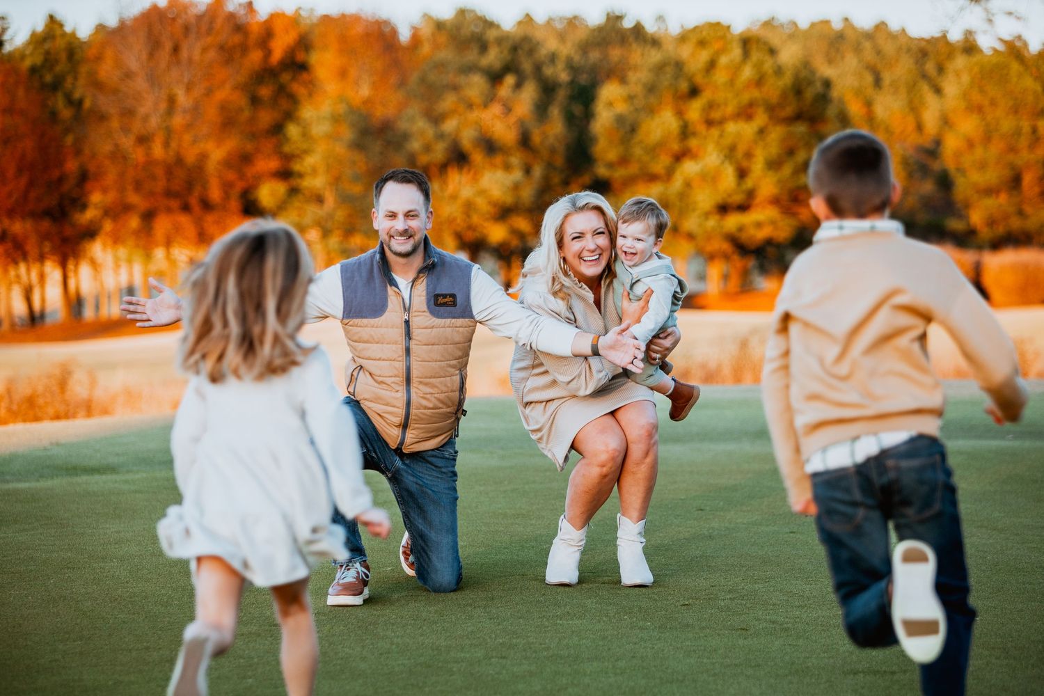 Parents kneeling on golf course as two children run toward them in fall.