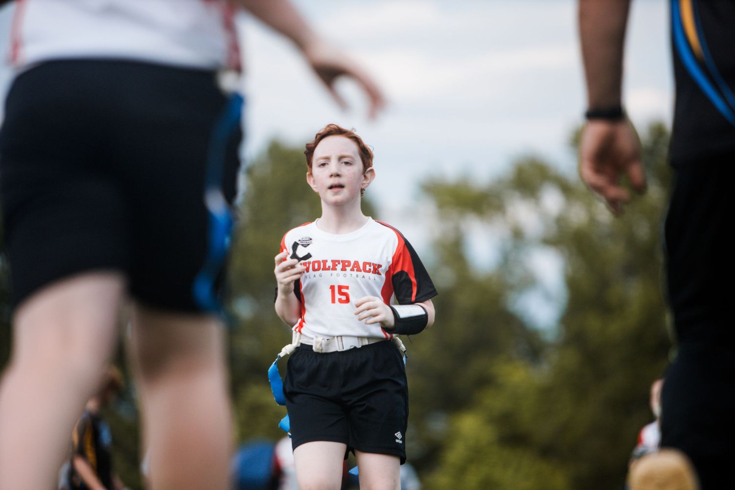 Young girl wearing Wolfpack #15 jersey running during a flag football game.