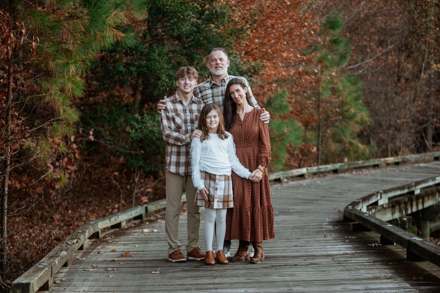 Family of four posing on wooden boardwalk surrounded by vibrant autumn foliage.