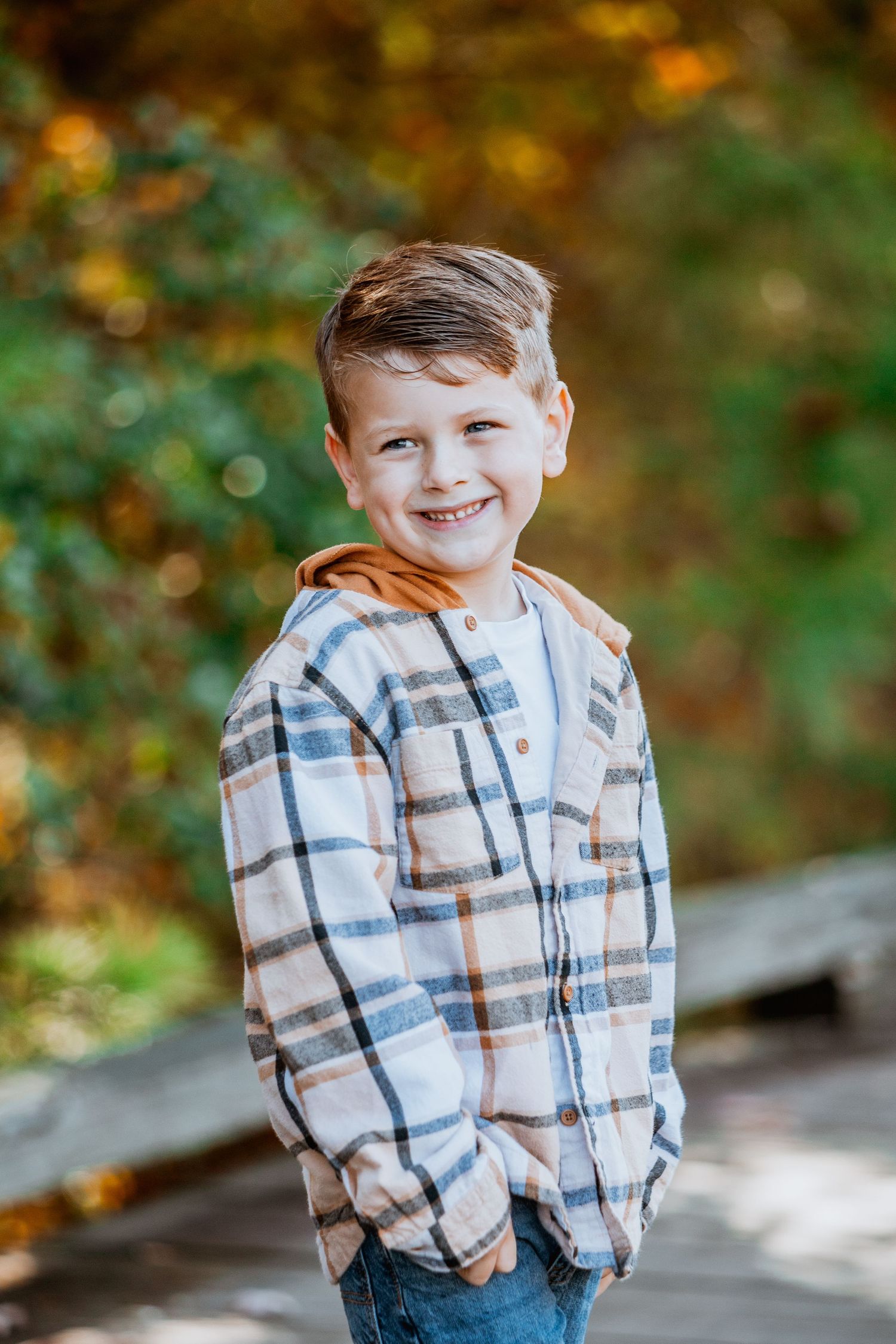 Happy boy in plaid shirt with orange hoodie smiling during fall outdoor portrait session.