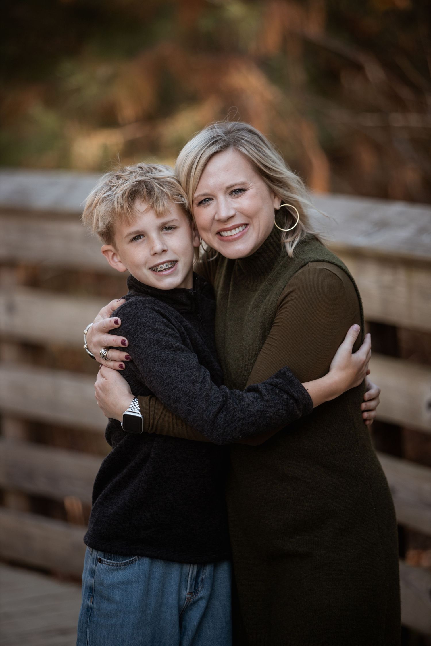 Blonde woman and young boy sharing a warm hug on a wooden bridge in fall.