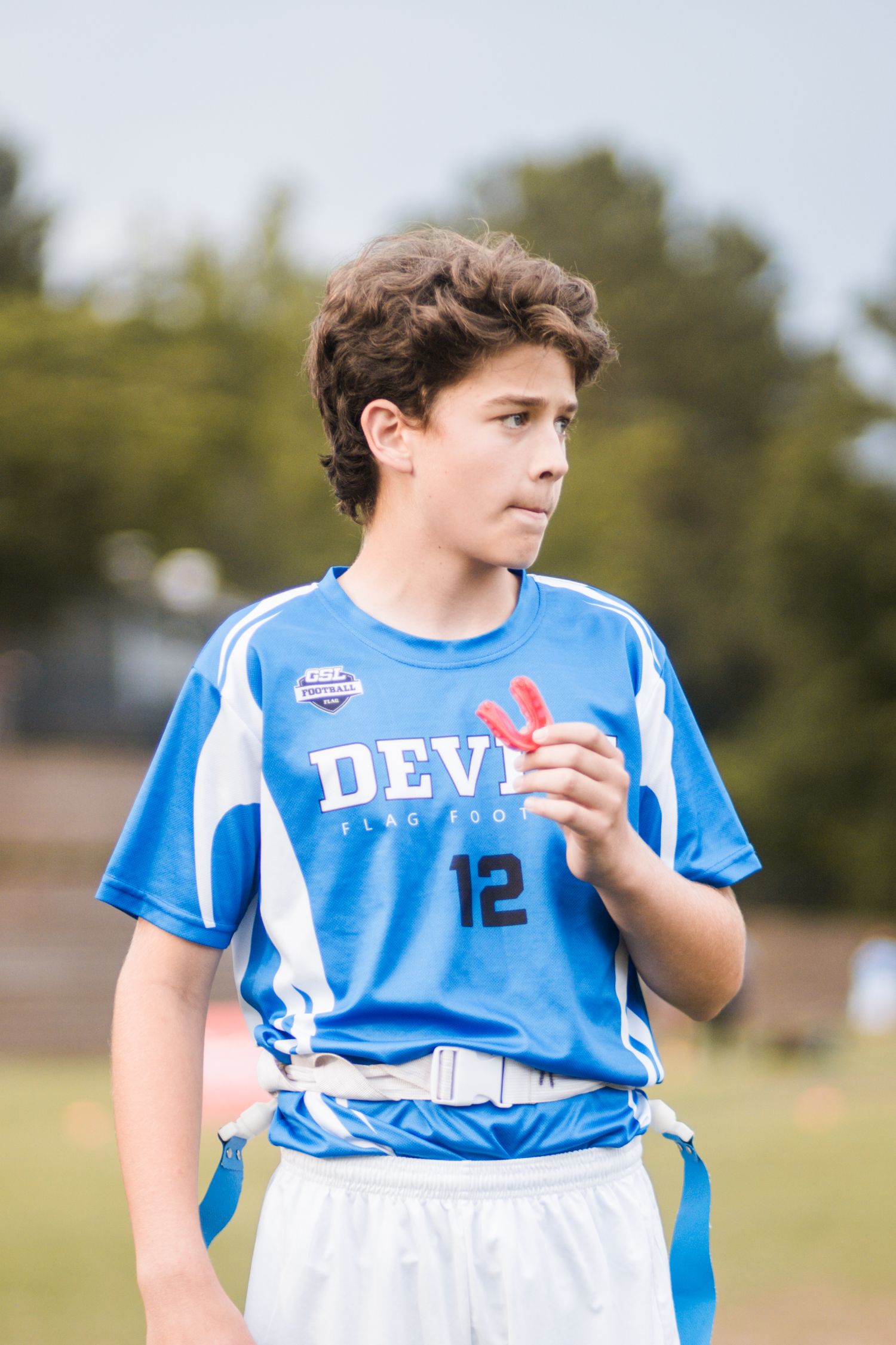 Teen athlete number 12 in blue Devils flag football uniform holding red mouthguard.
