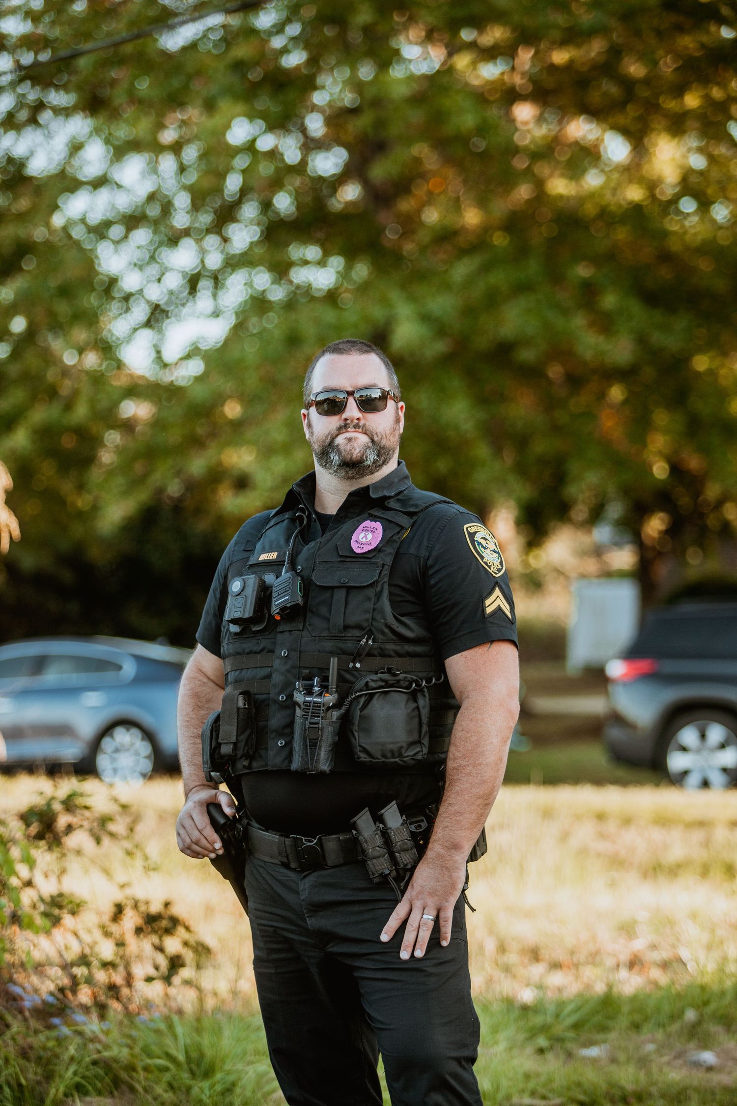 Police officer in tactical gear and sunglasses standing outdoors.